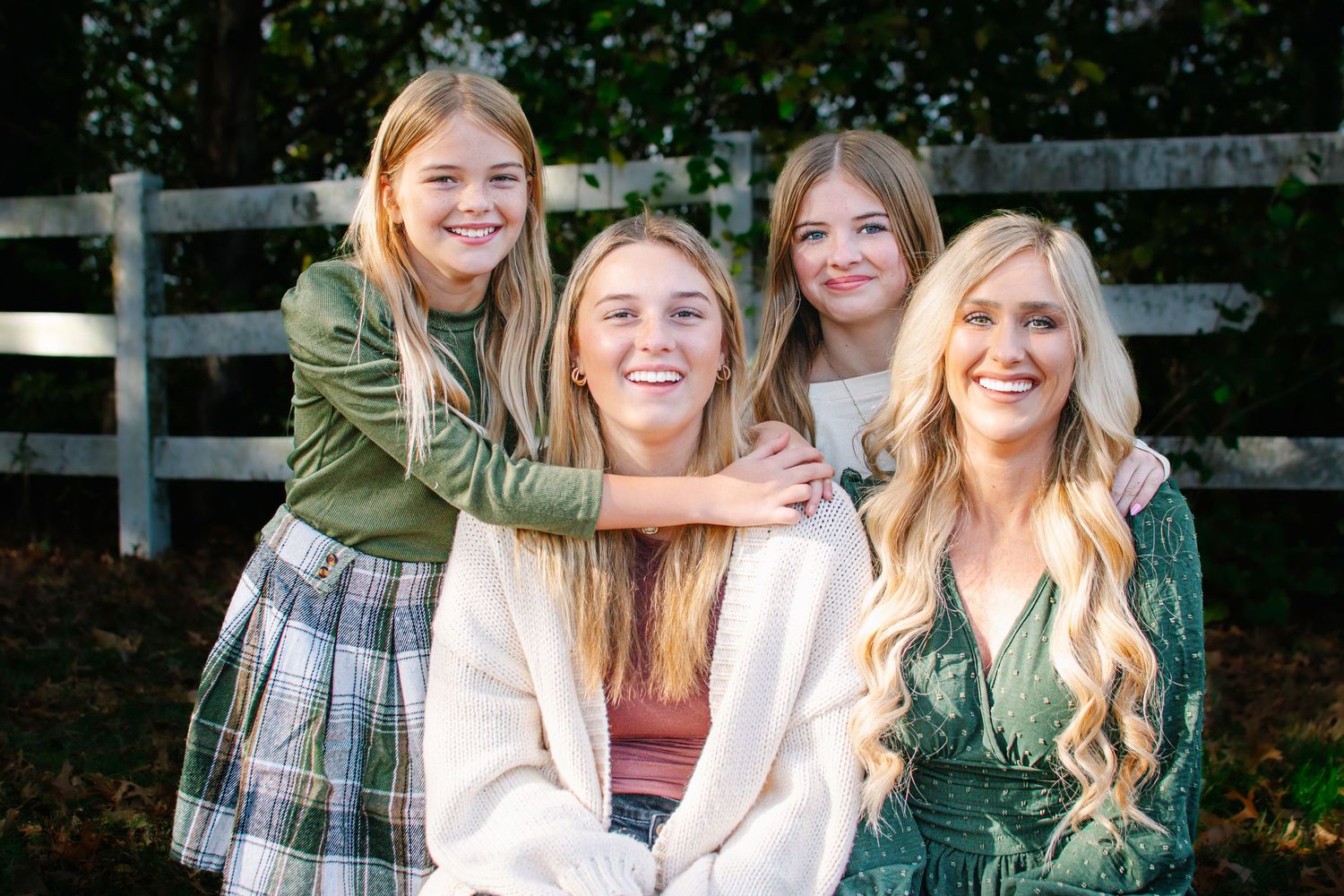 Four smiling blonde girls pose together outdoors in coordinating green and white outfits.
