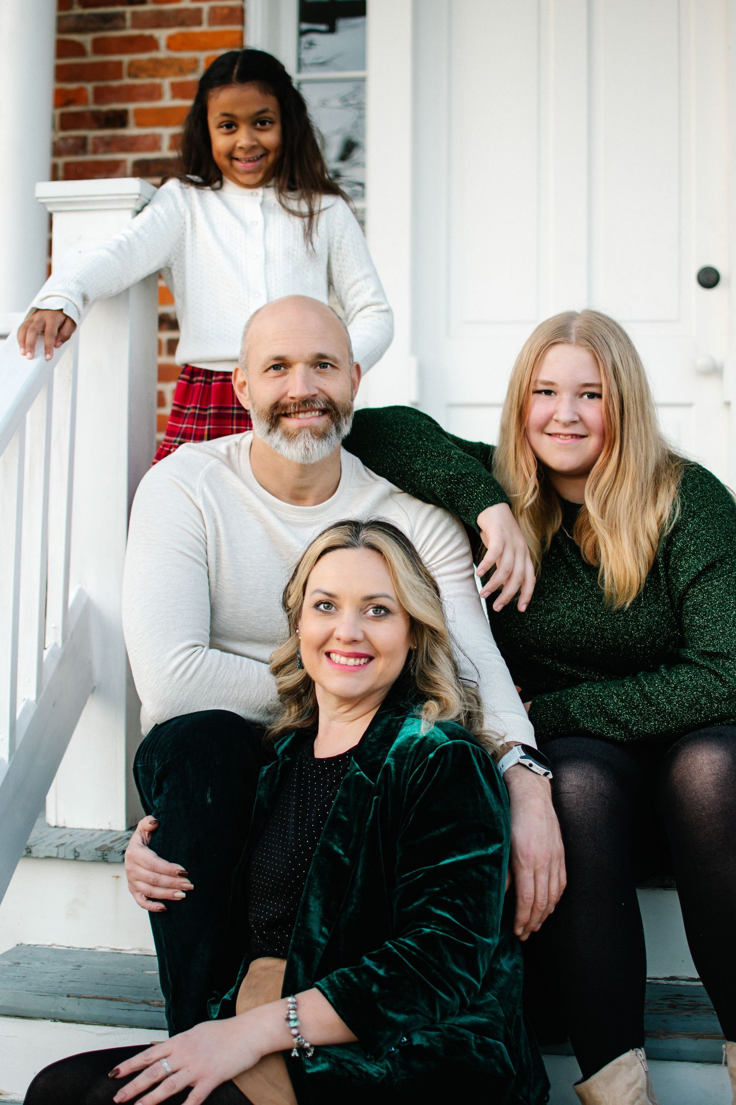 A family of four poses on white porch steps in coordinated green and cream holiday outfits.
