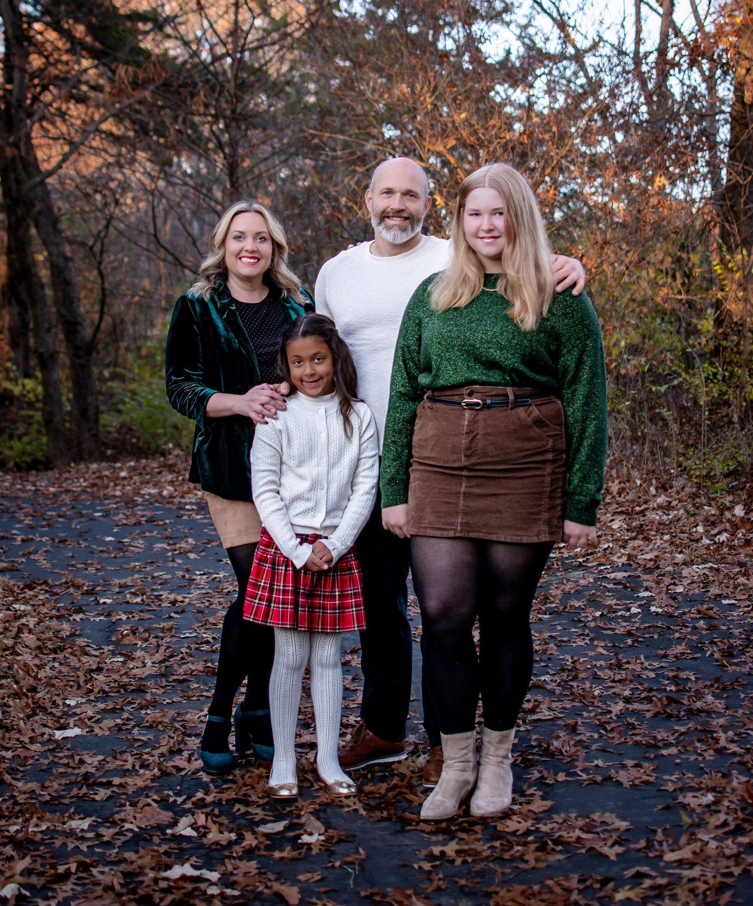 A family of four poses together on a leaf-covered path during a fall outdoor photo session.