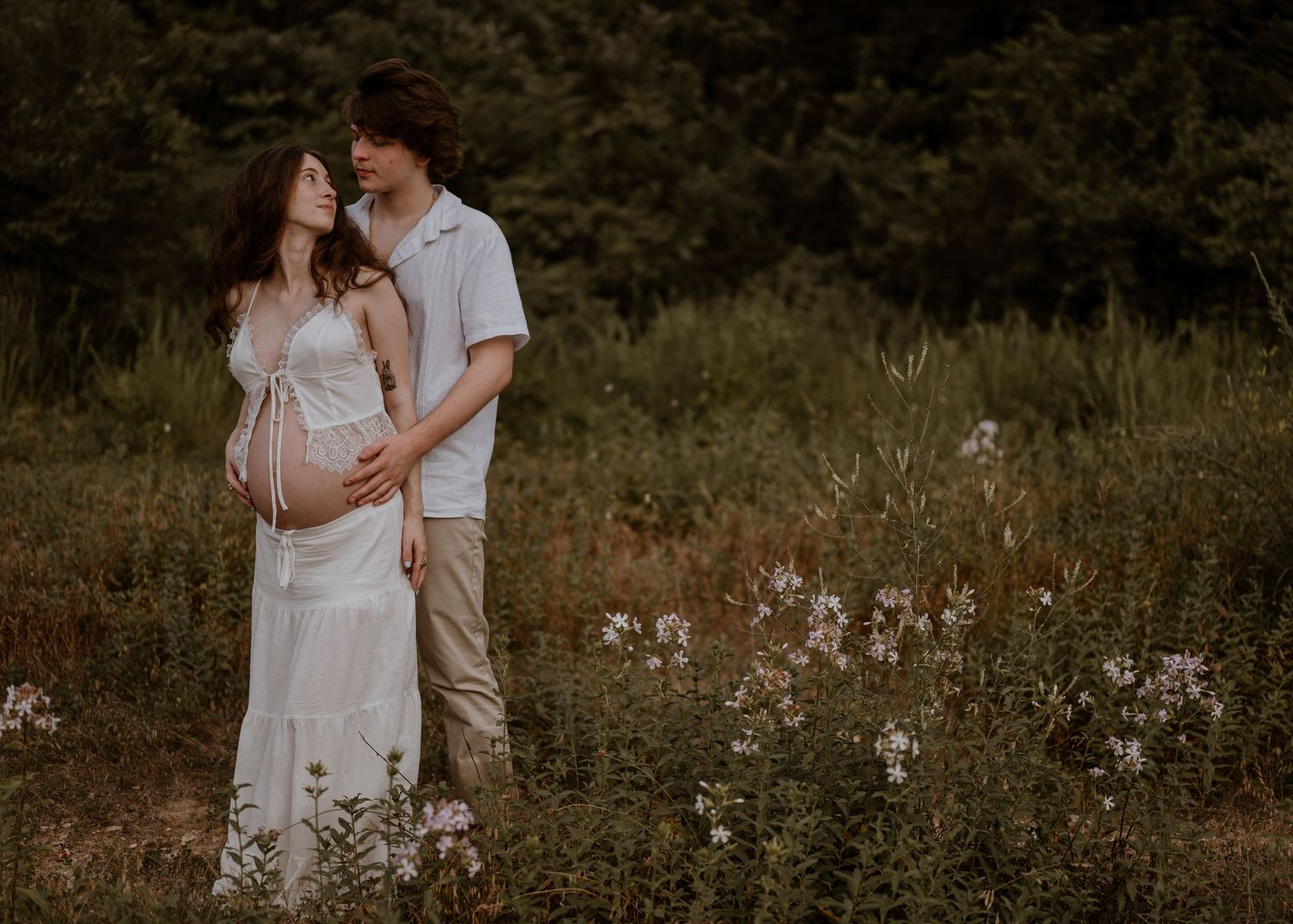 A couple shares a tender embrace in a wildflower field during a dreamy outdoor maternity photography session.