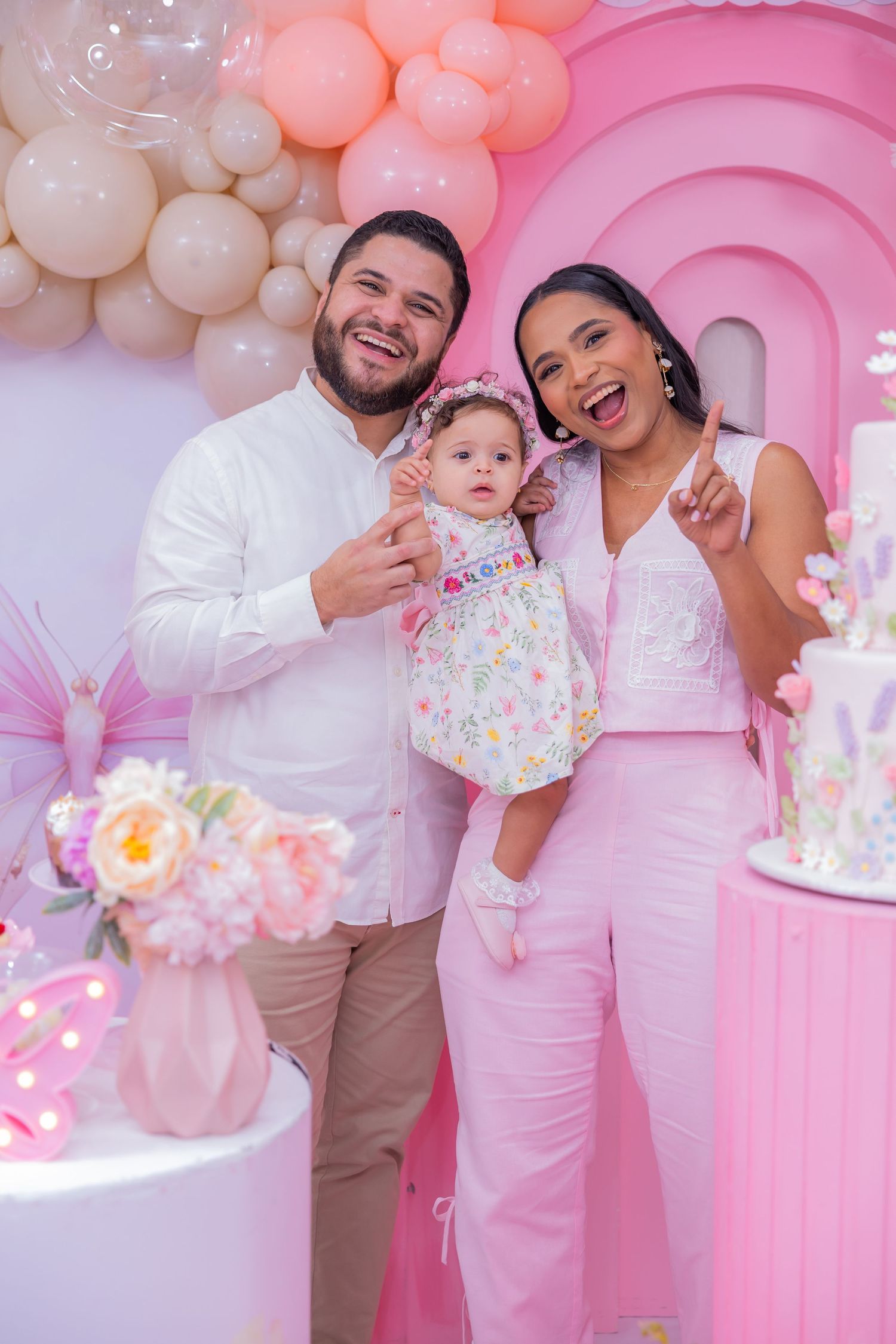 A family celebrates at a pink and white themed party with balloon decorations and a festive atmosphere.