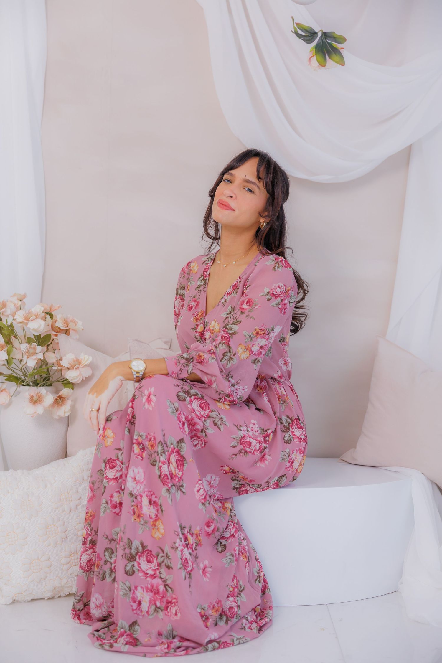 Woman in pink floral maxi dress sitting gracefully in a soft white studio setting.