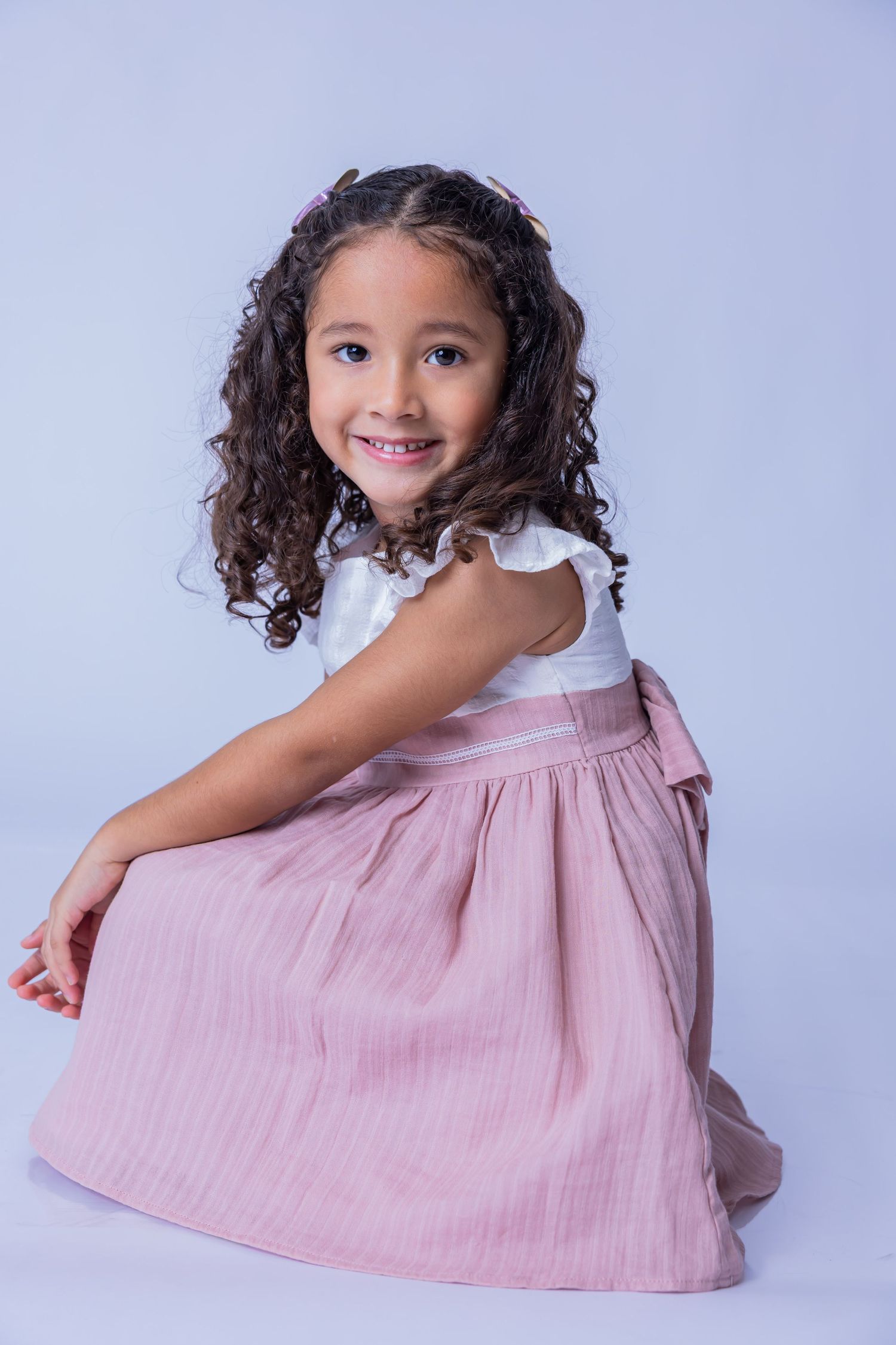 A child in a pink dress twirls and poses playfully against a light blue studio backdrop.