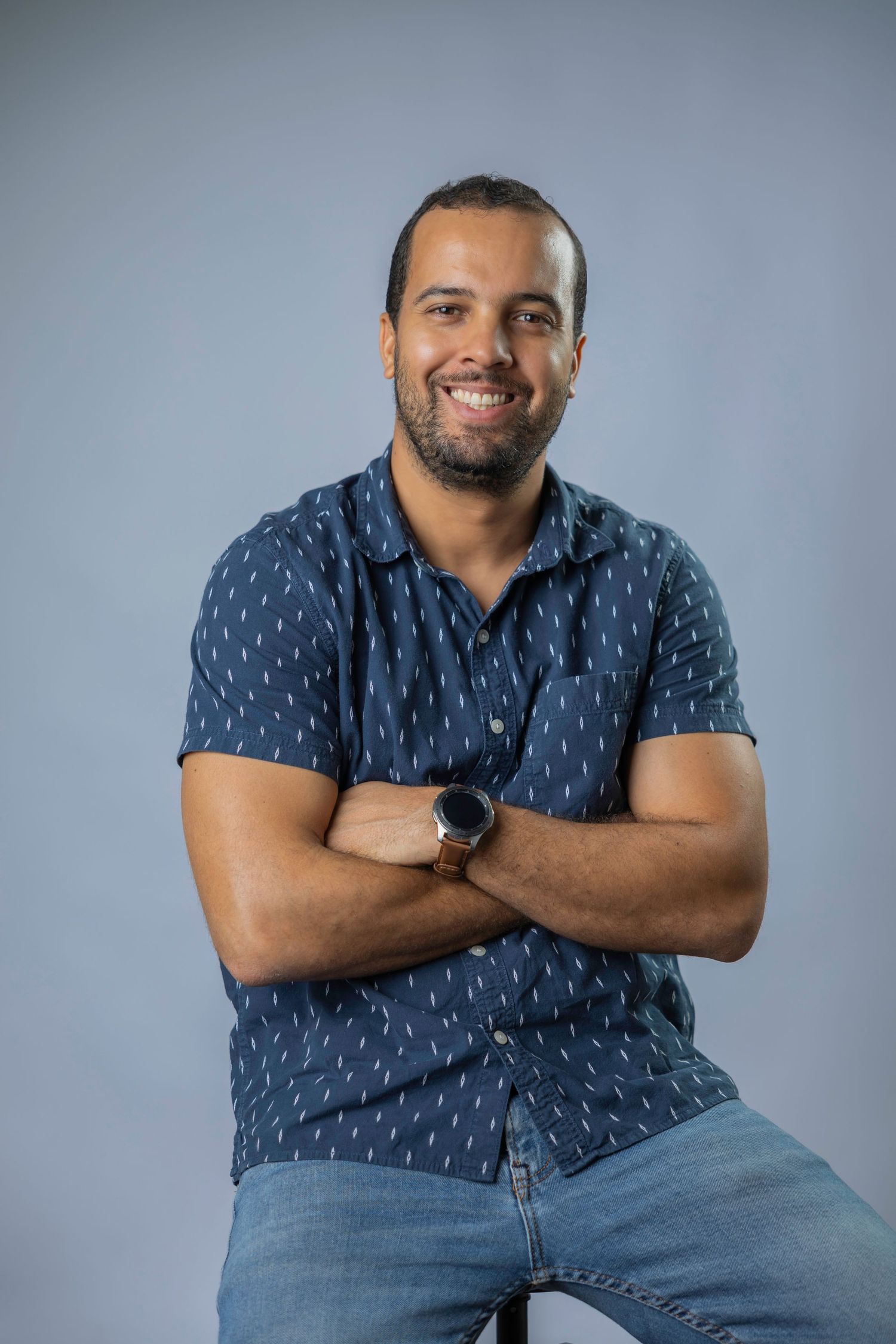 Person in blue patterned shirt and jeans poses against gray background in professional portrait series.