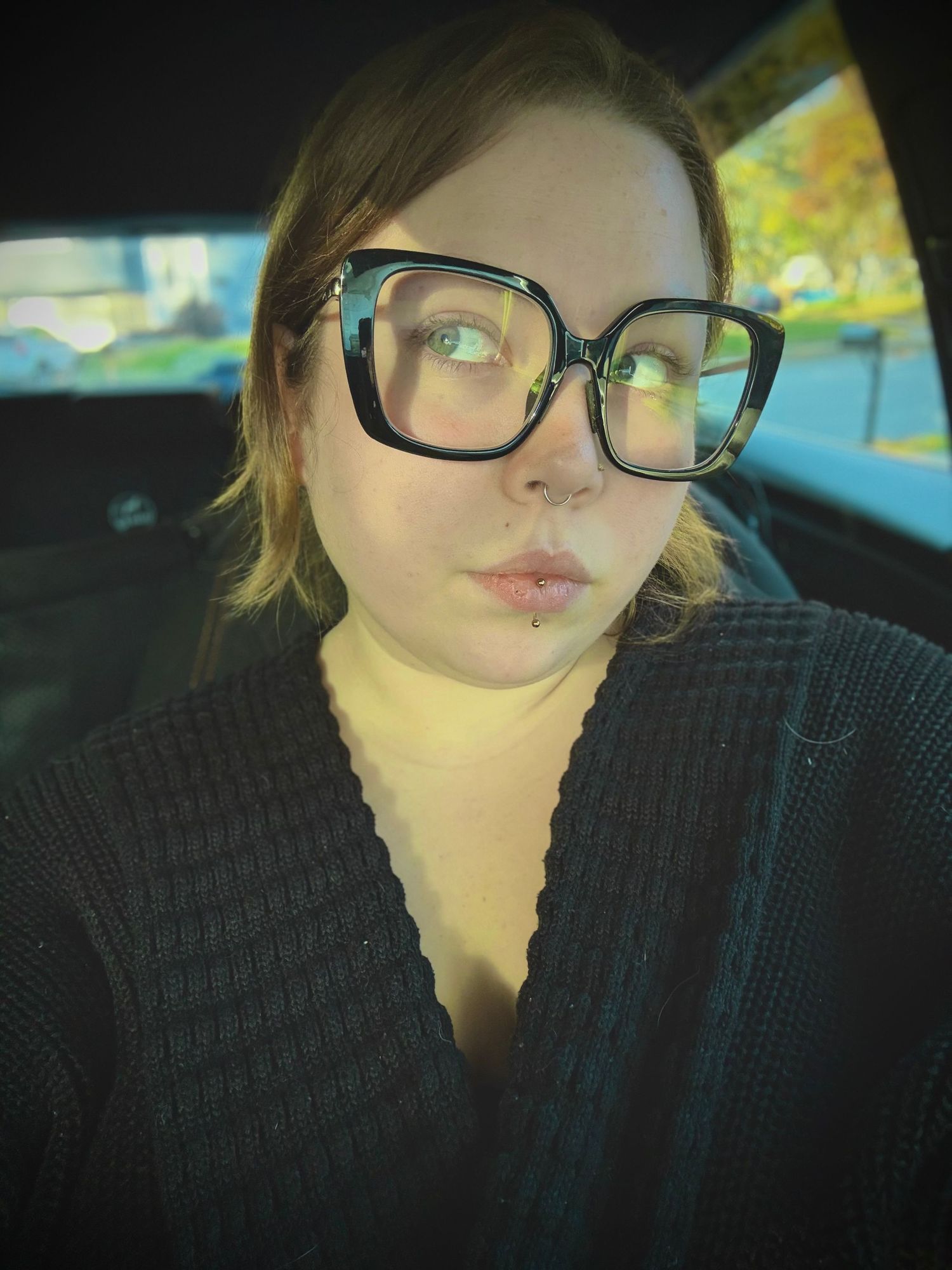 Person wearing glasses resting in car interior with natural lighting.