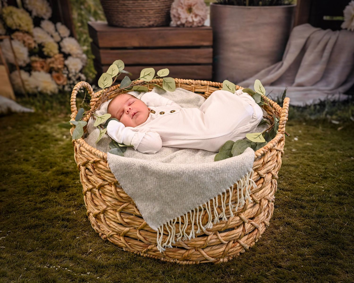 Newborn baby sleeping peacefully in a wicker basket with green leaves and a soft blanket.