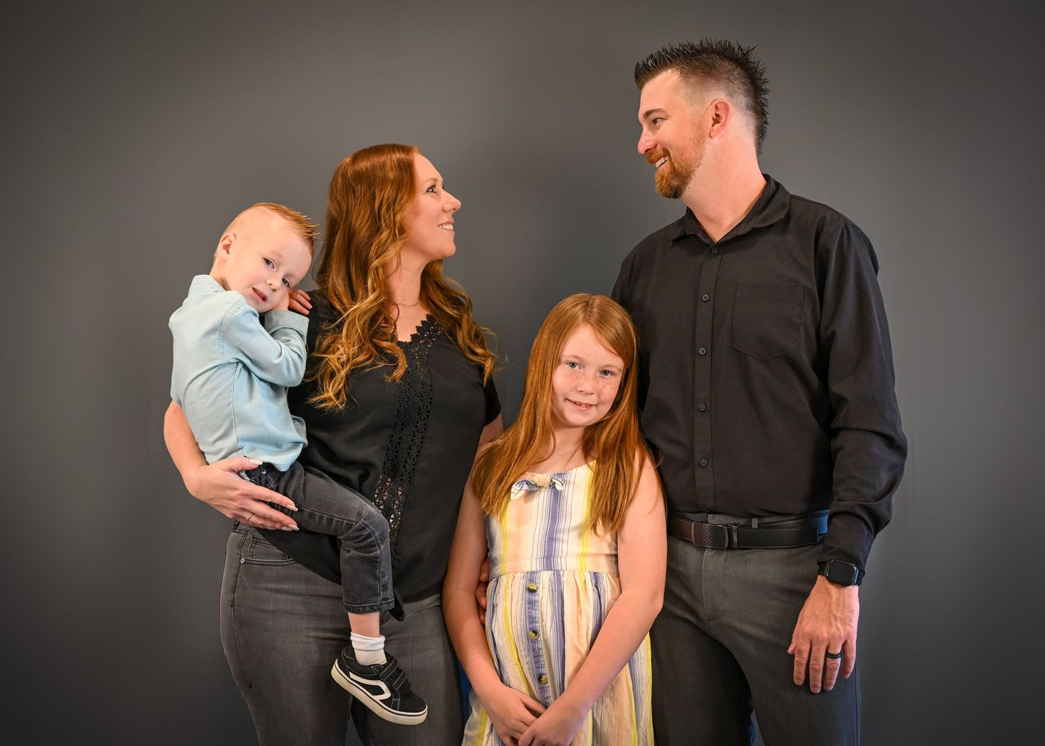 Professional studio portrait series showing a family of four in coordinated dark outfits against a grey backdrop.