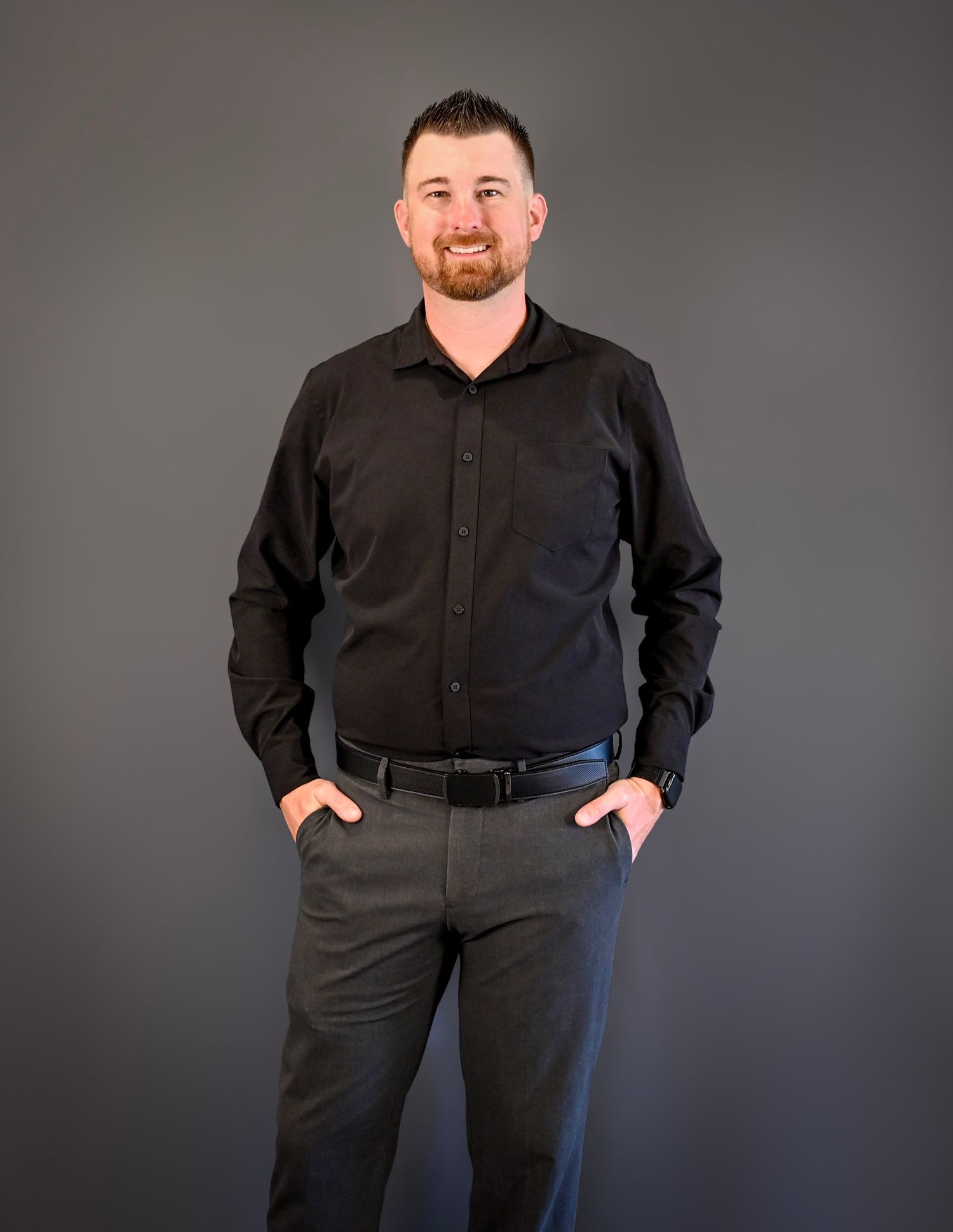 Professional studio portrait showing a person in all black attire against a gray backdrop.