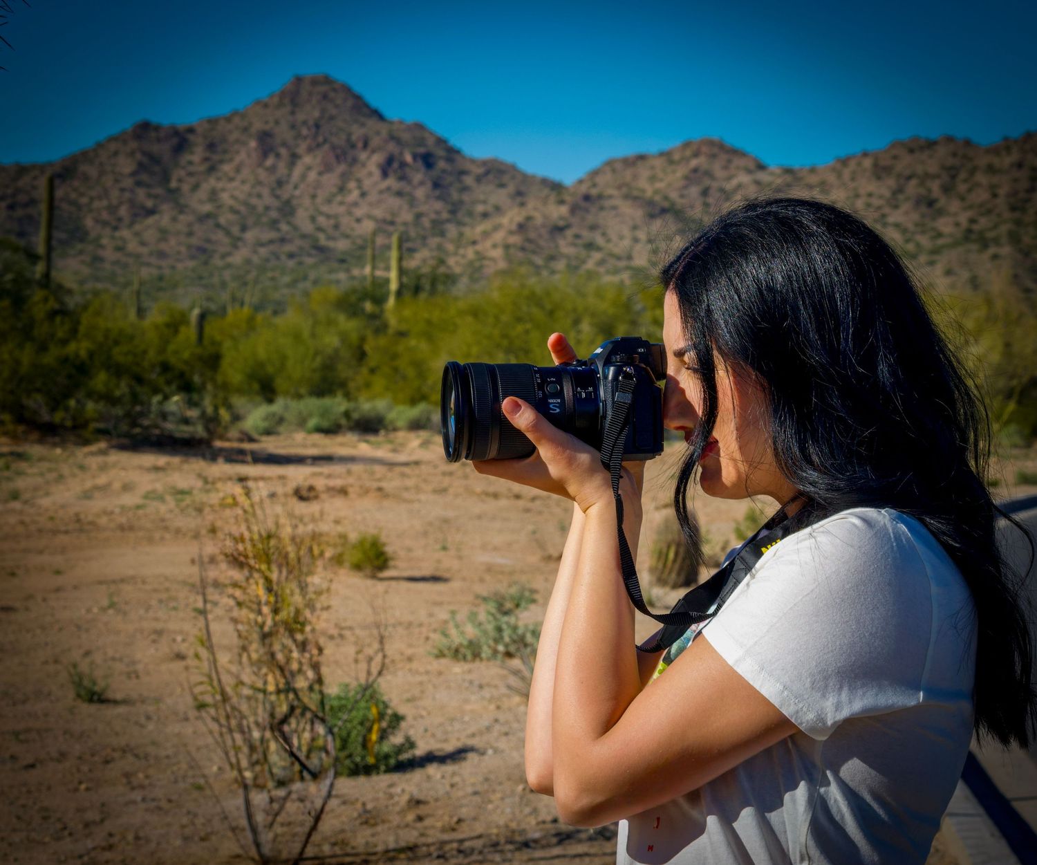 Photographer shooting in a scenic desert setting with mountain backdrop and native plants.