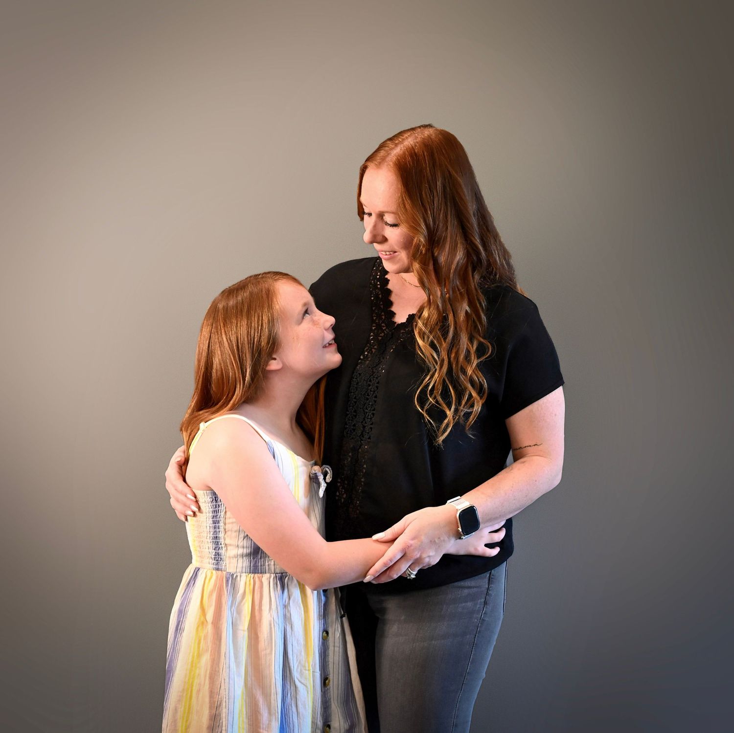 A tender moment captured between two people with red hair sharing a warm embrace against a neutral backdrop.