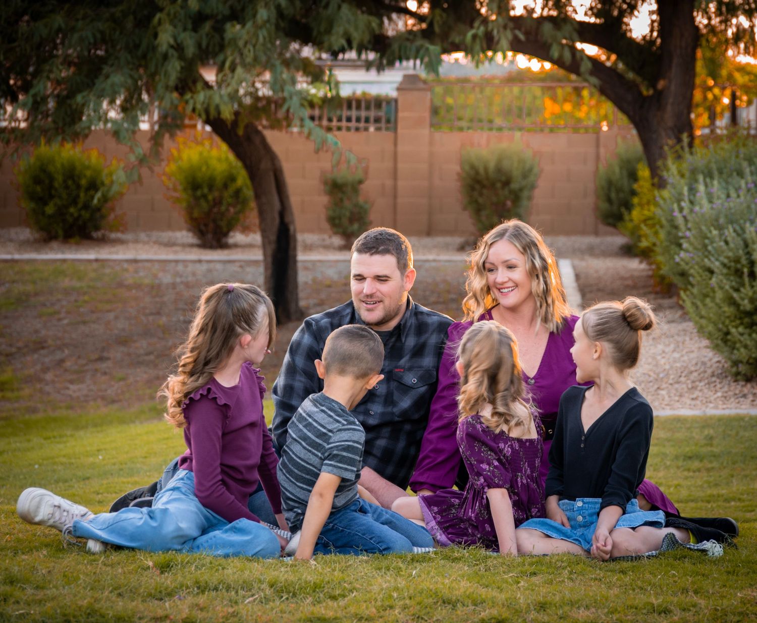 Family portrait session on grass with autumn trees and warm sunset lighting.