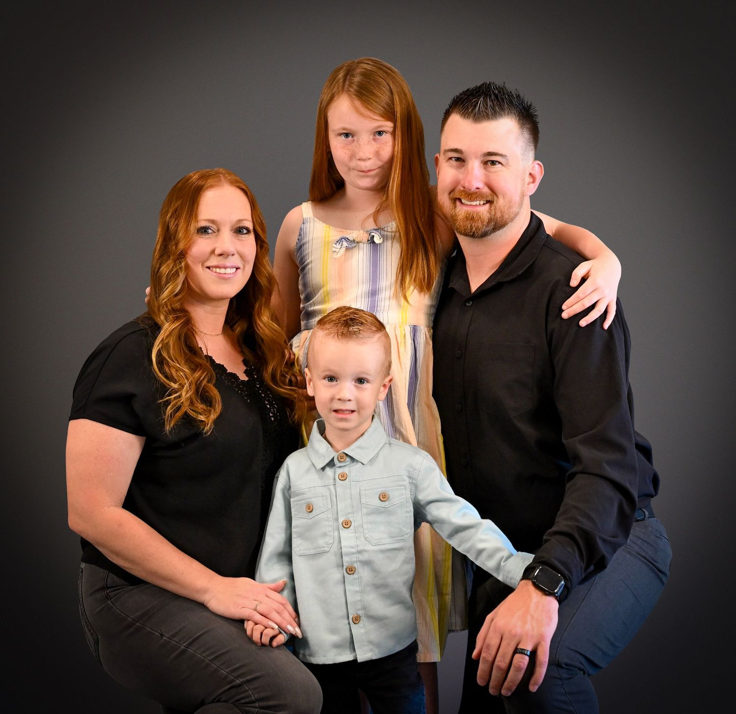 A family portrait against a dark background showing parents and two children in coordinated black and blue outfits.