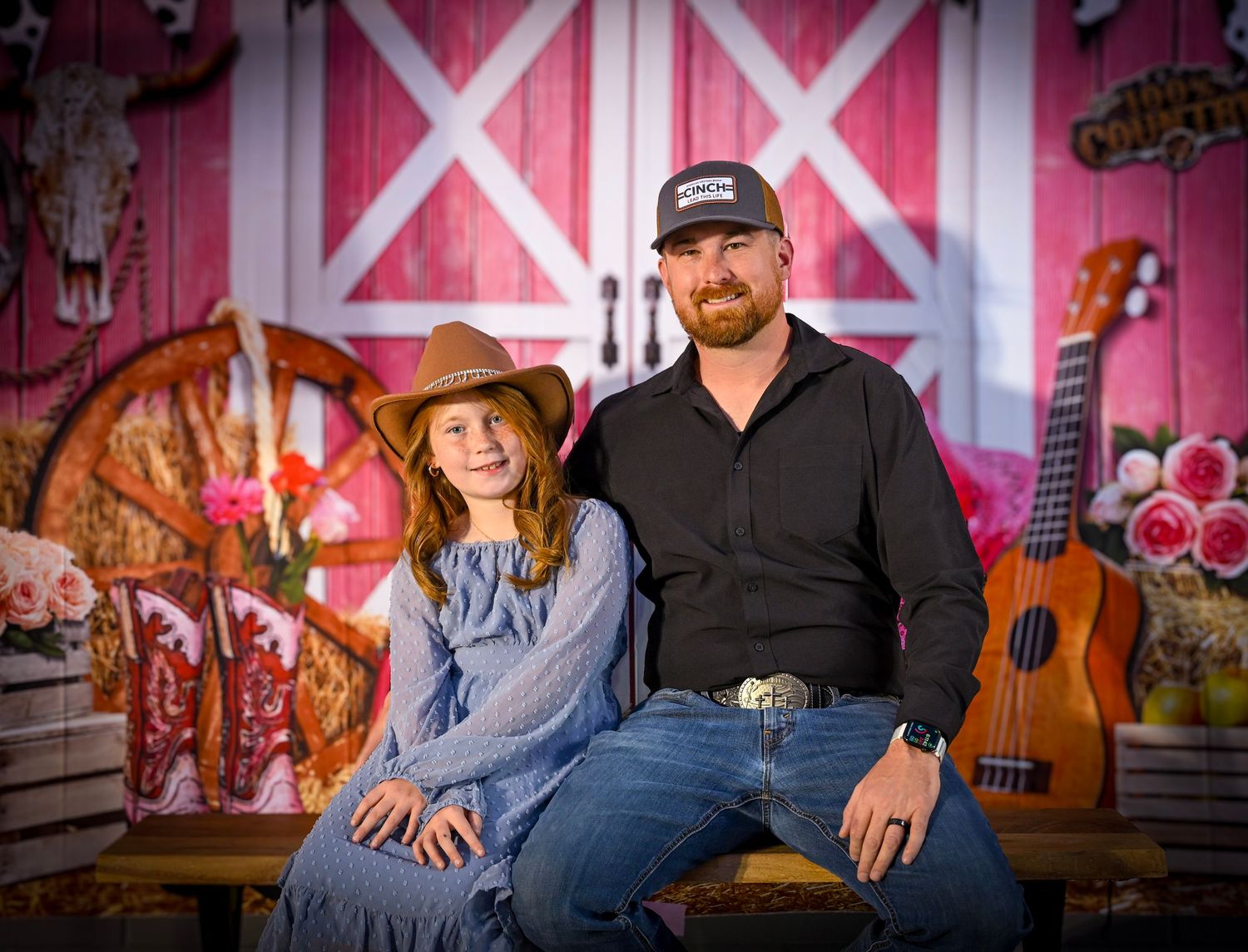 A couple poses together in front of a rustic red barn wall with musical instruments.