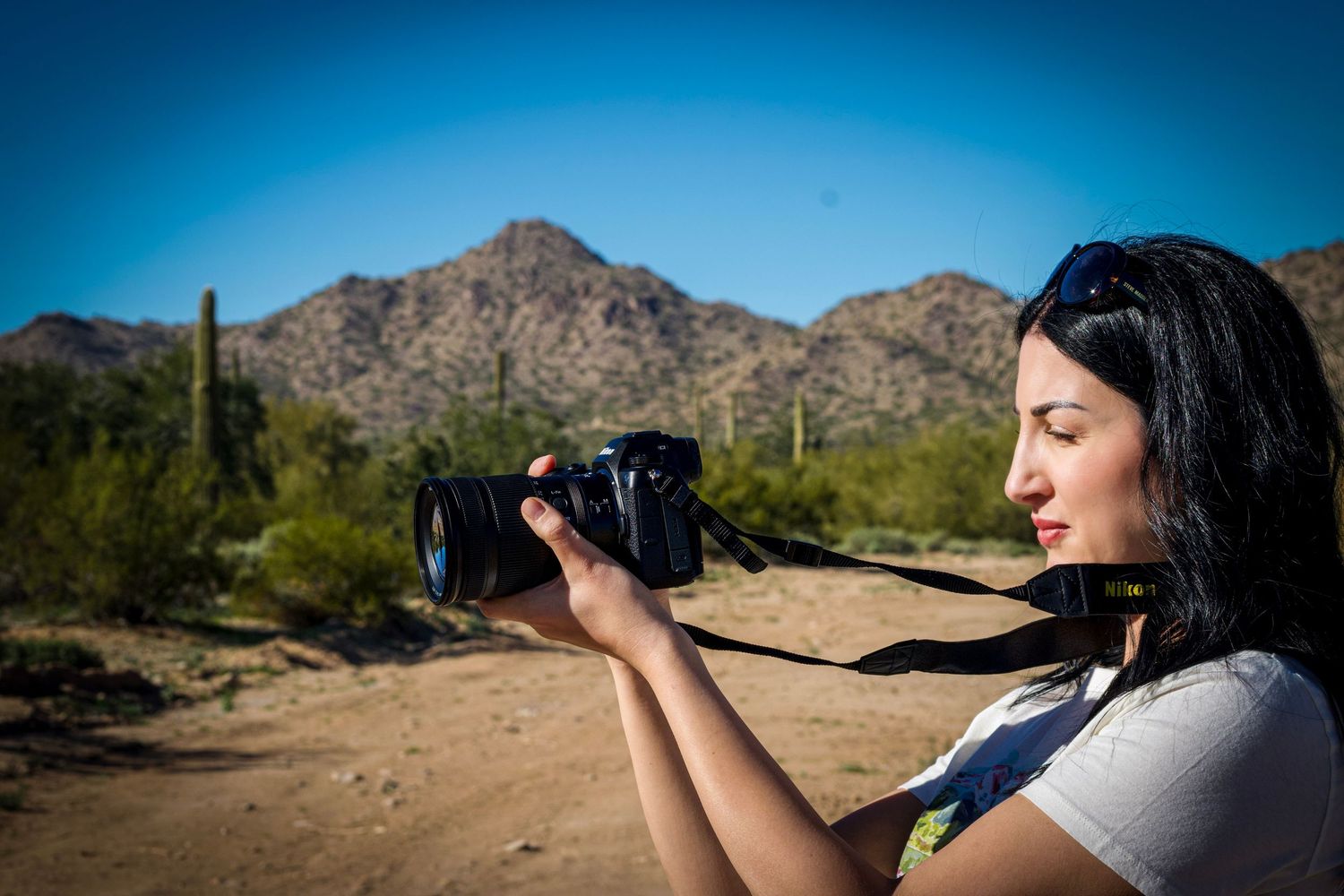 A photographer captures images in a desert landscape with mountains and saguaro cacti in the background.