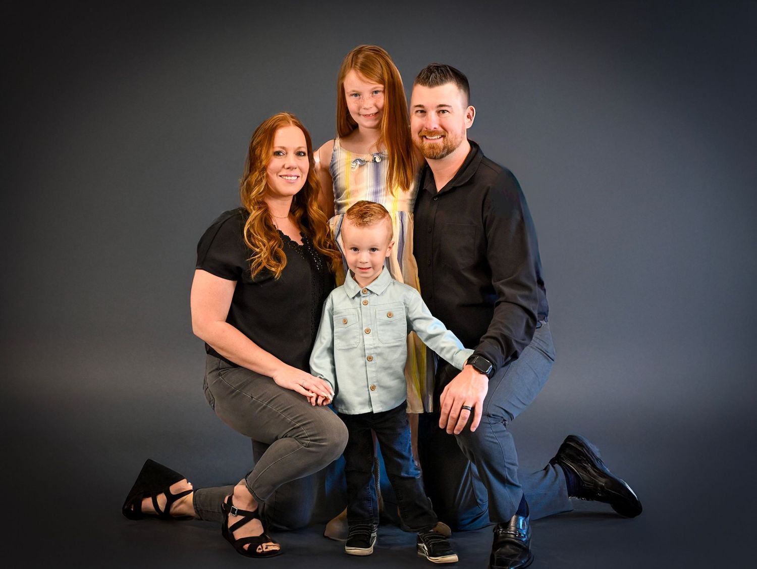 Family portrait session in studio with three people against dark background showing warm connections.