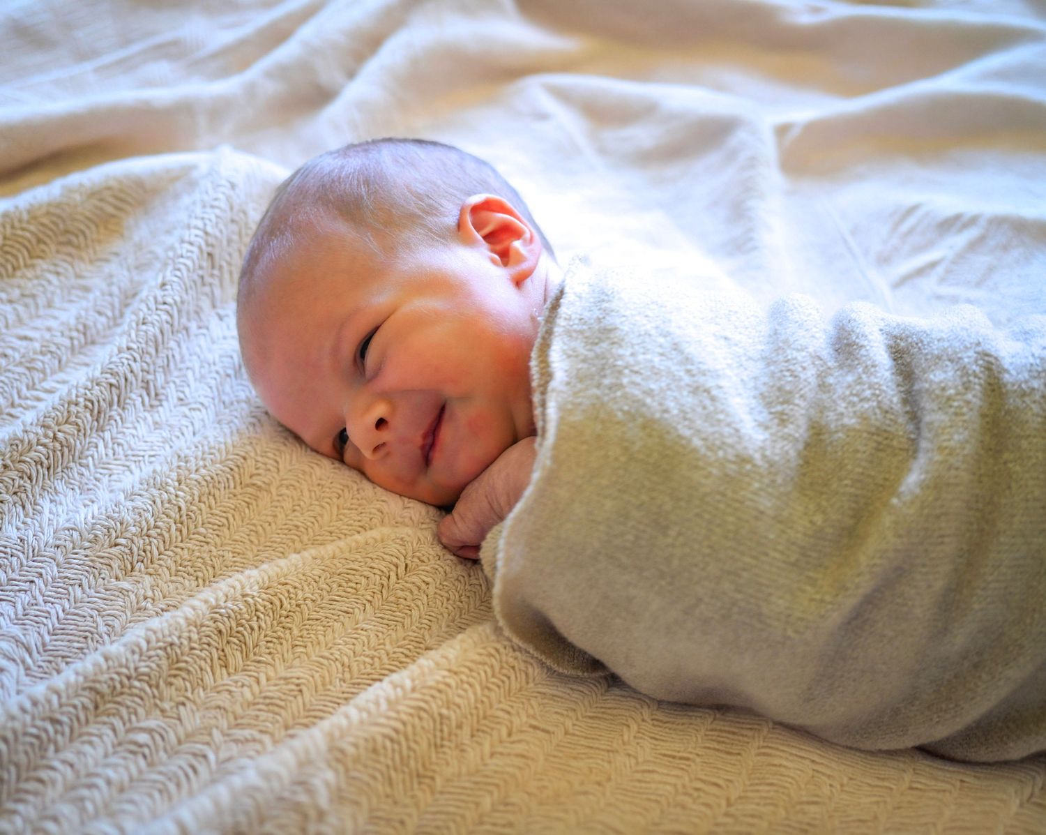 Peaceful newborn baby swaddled in a soft white blanket sleeping on a bed.