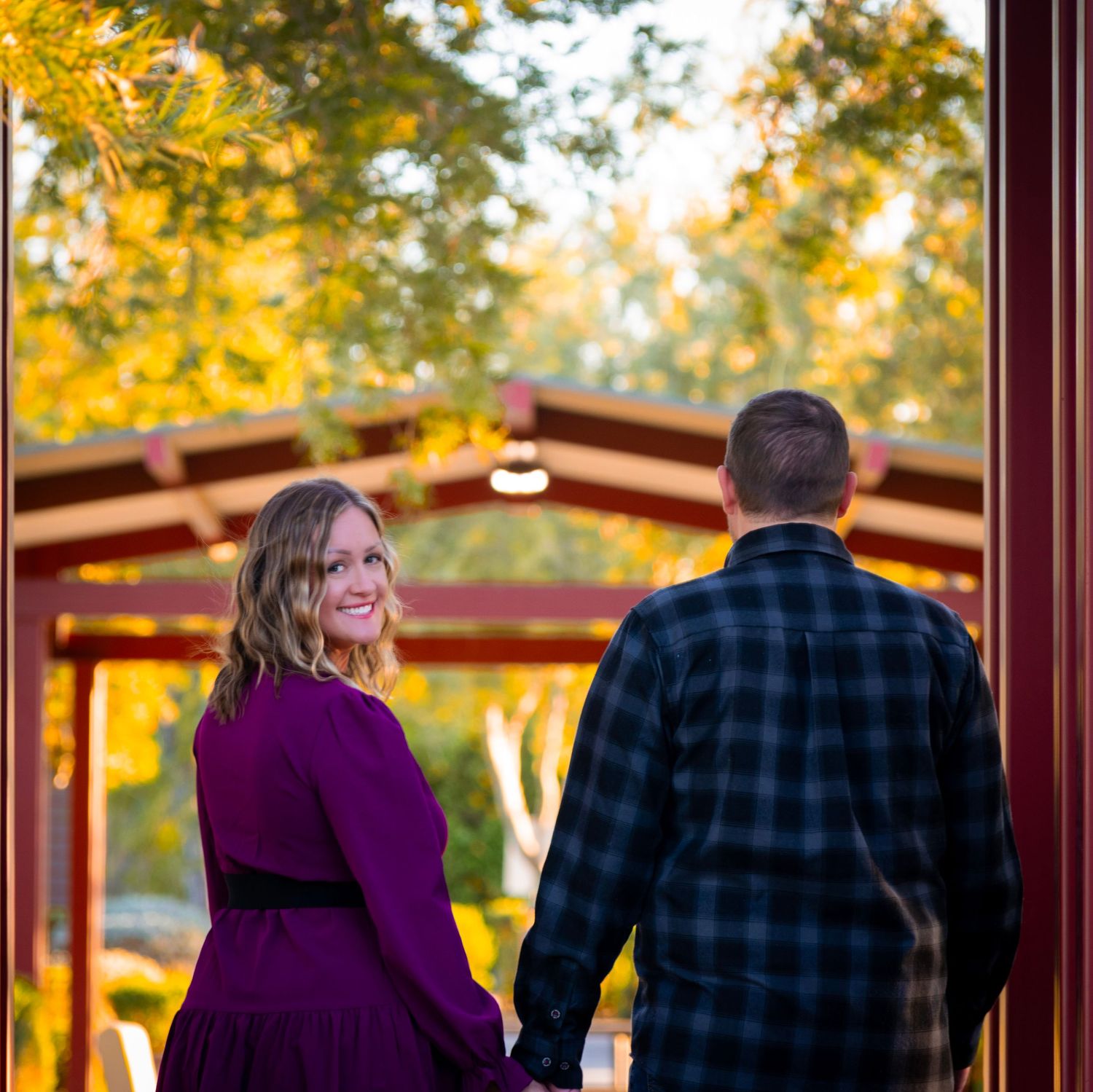 A couple stands together in a covered walkway during golden autumn sunset.