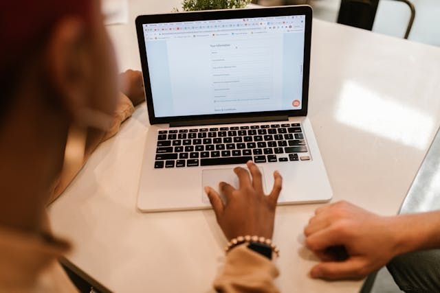 A person types on a laptop keyboard while working at a desk with documents and papers spread out.
