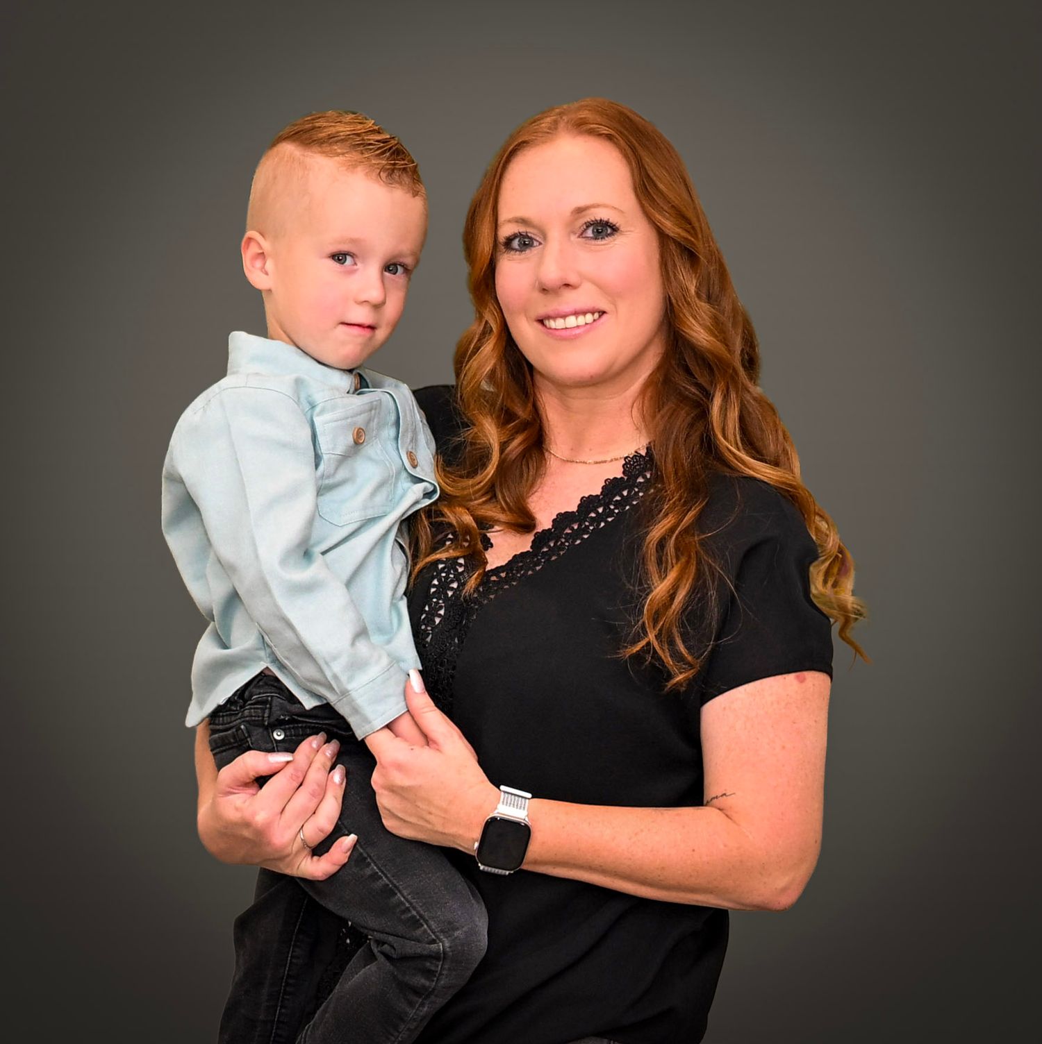 Professional studio portrait against dark background showing tender family moment in matching black and light blue outfits.