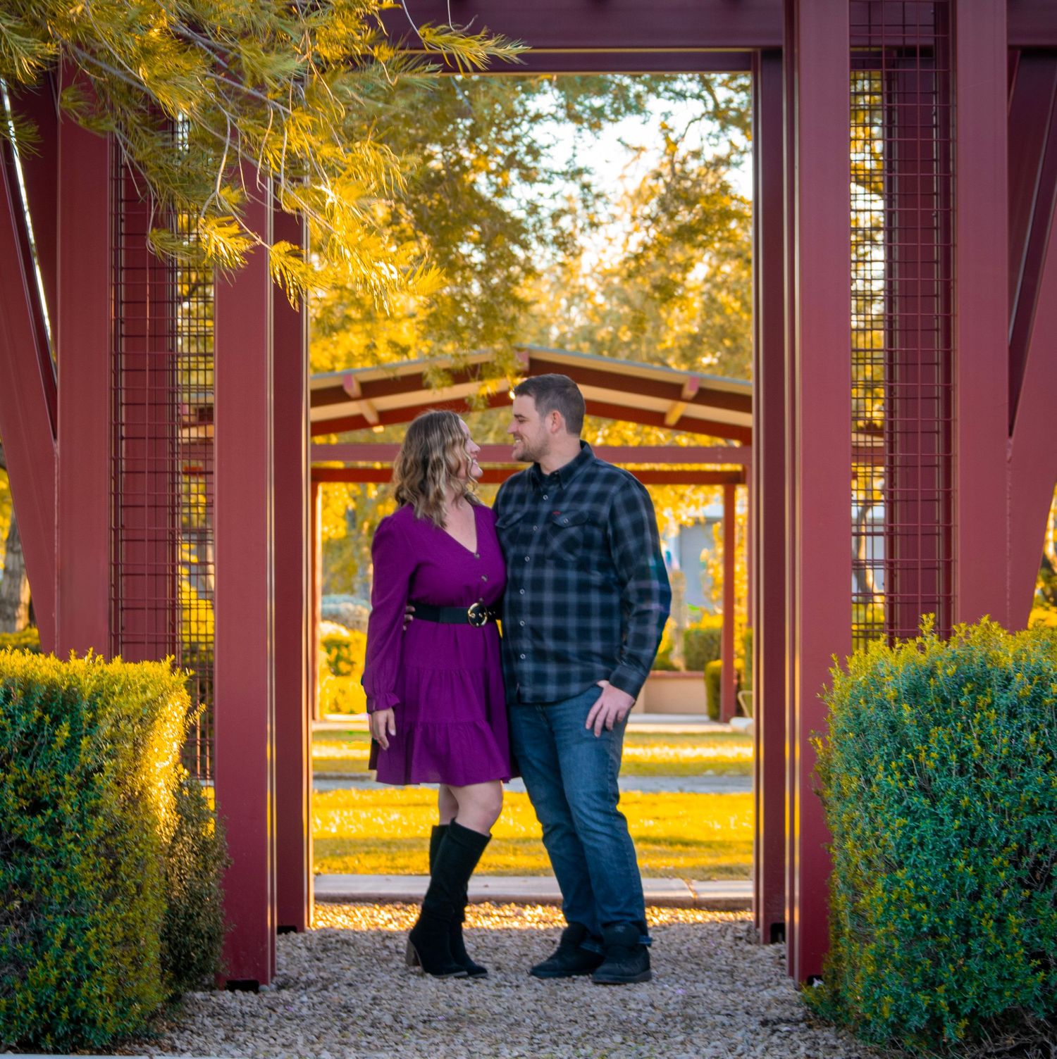 A romantic autumn scene in a covered walkway with red pillars and green shrubs.