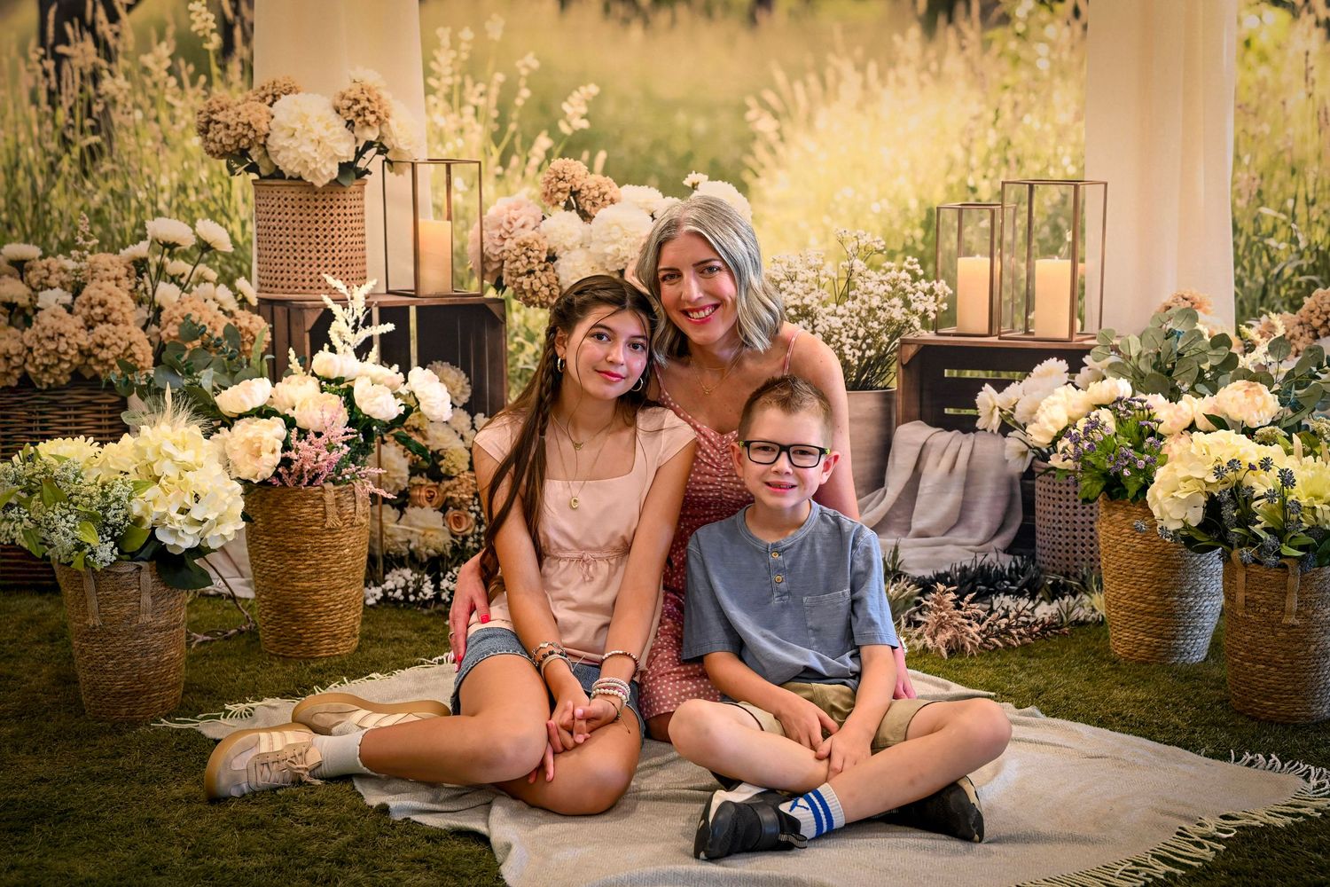 Woman and two children sitting on blanket surrounded by white floral arrangements in a garden portrait setting.