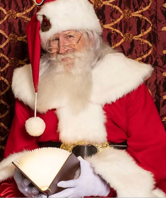 Santa Claus in a red suit reading an open book in a festive Queen Creek studio, perfect for family holiday photos.