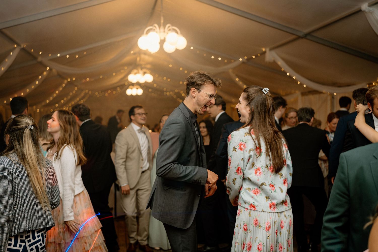 Couples dancing and mingling at a wedding reception under string lights and chandeliers.