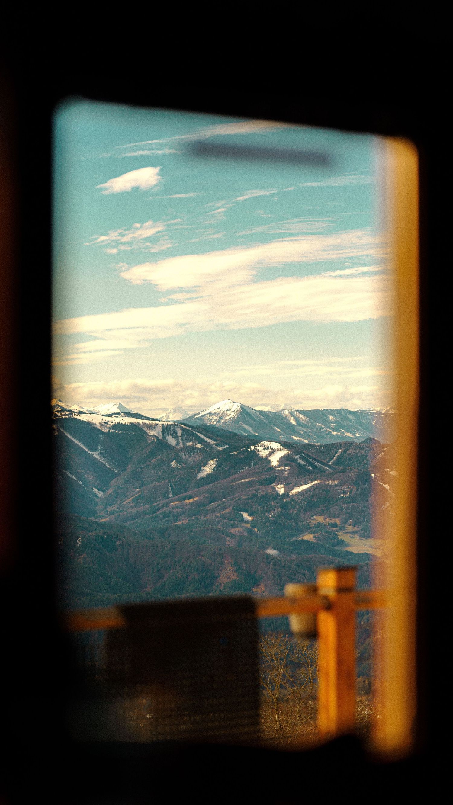 Snow-capped mountain peaks viewed through a window frame against a sunset sky.