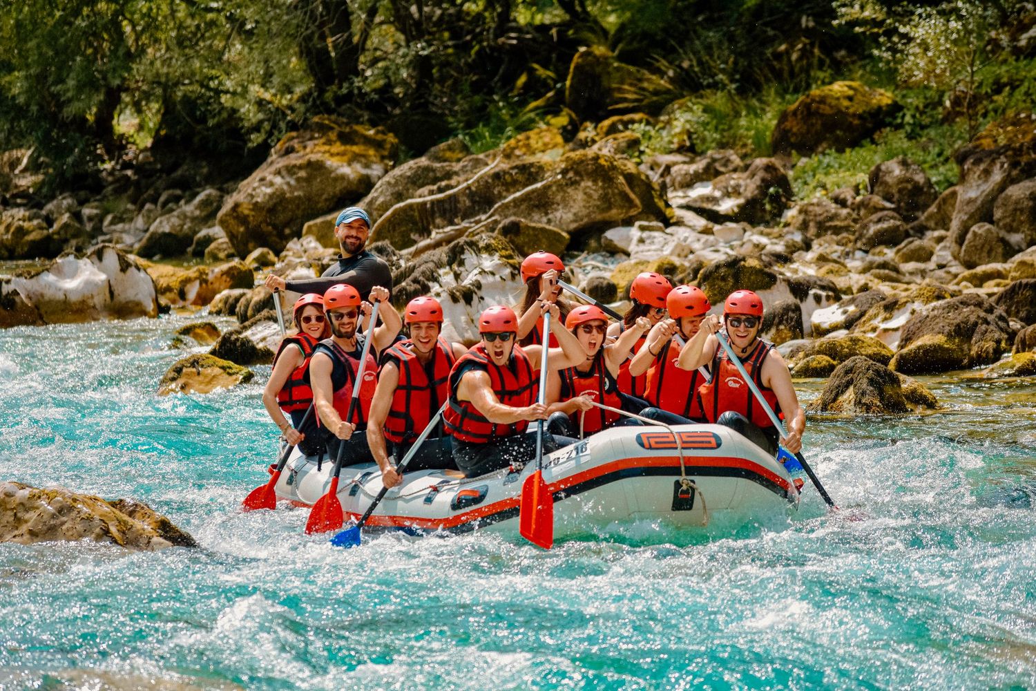 White water rafting group in red safety gear navigating turbulent blue rapids.