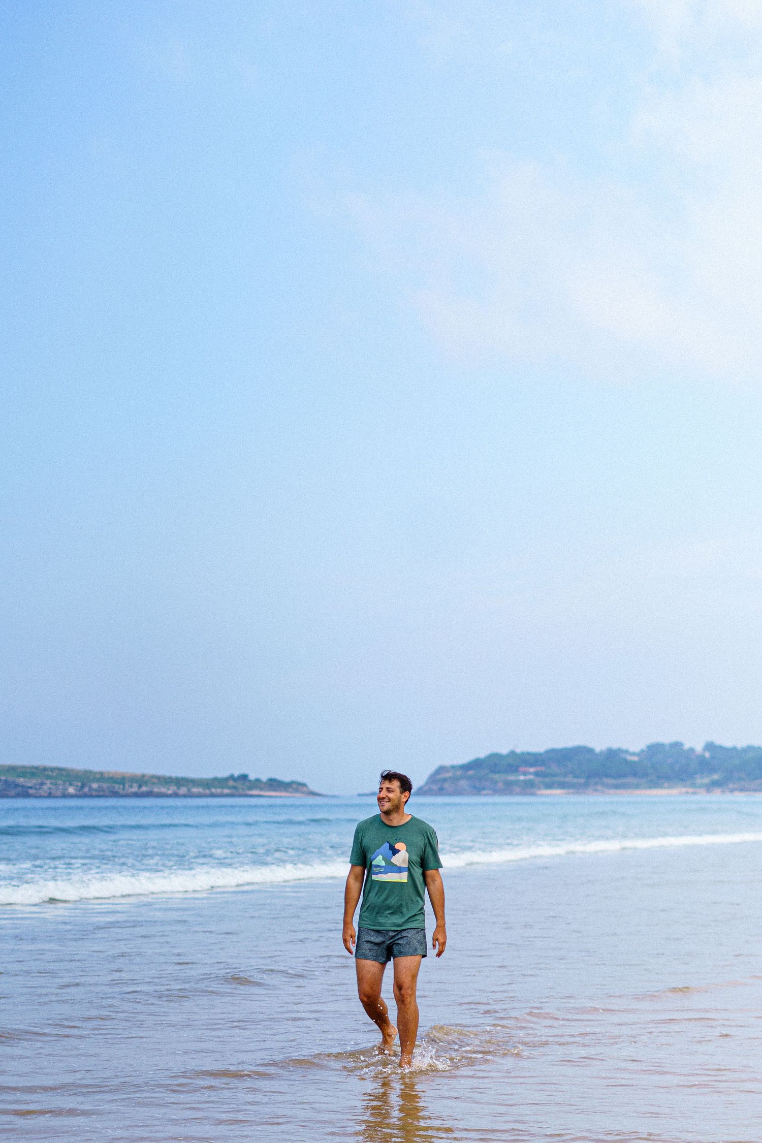 Person walking along the shoreline of a beach with blue ocean and sky in background.