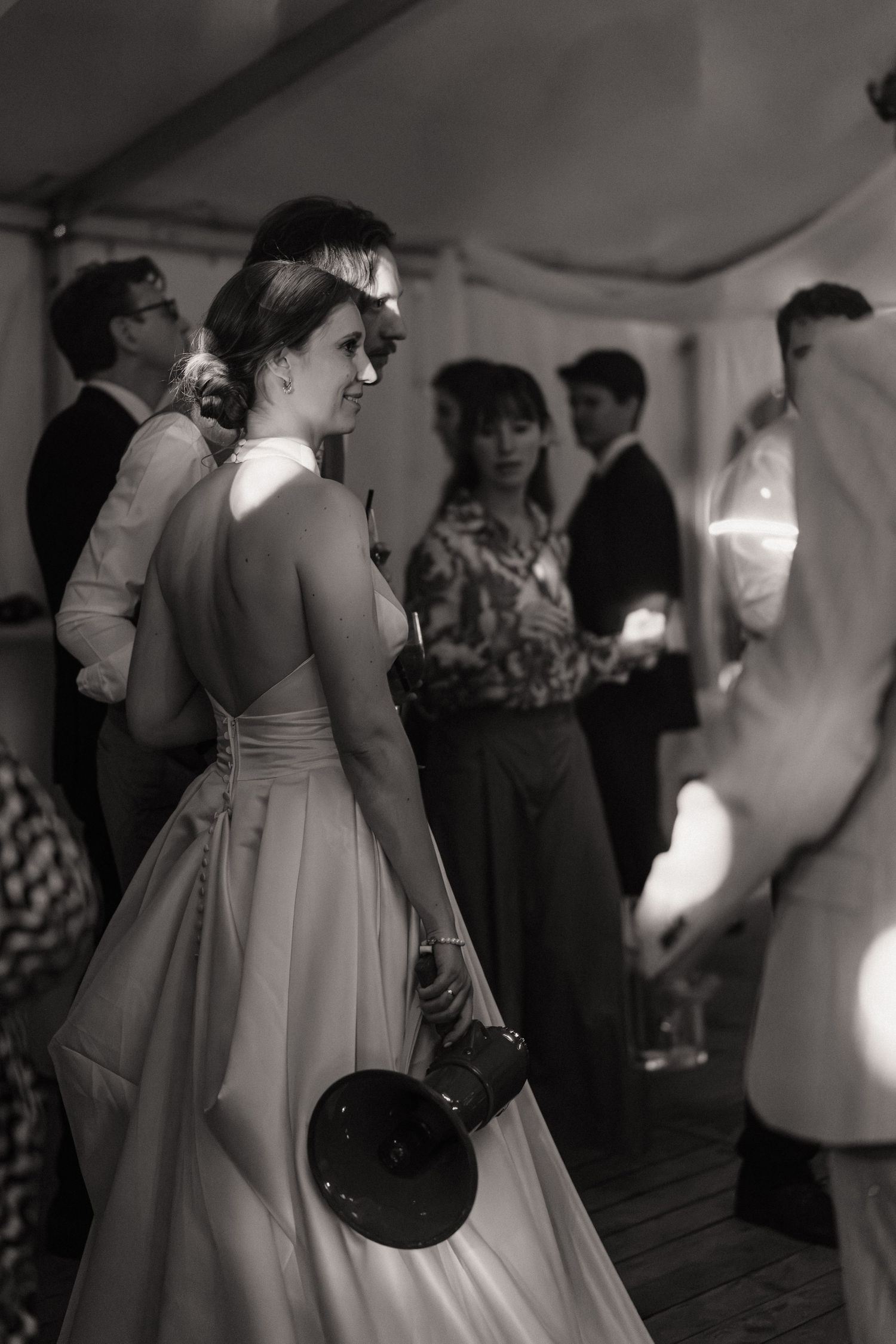 A guest in an elegant dress stands in profile at a dimly lit wedding reception.