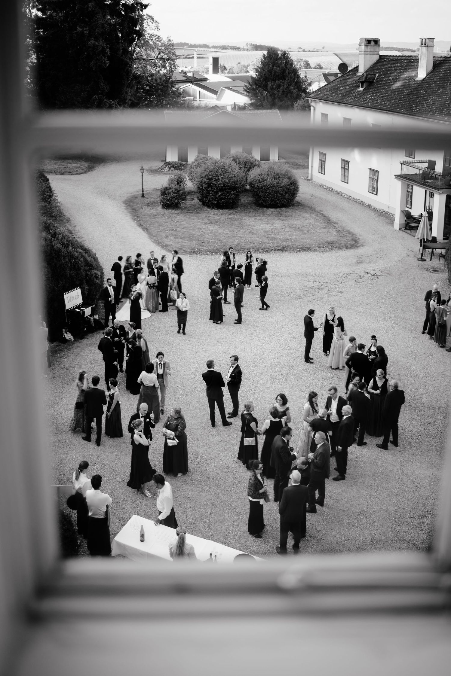 Black and white aerial view of elegantly dressed guests mingling outdoors at a formal garden party event.