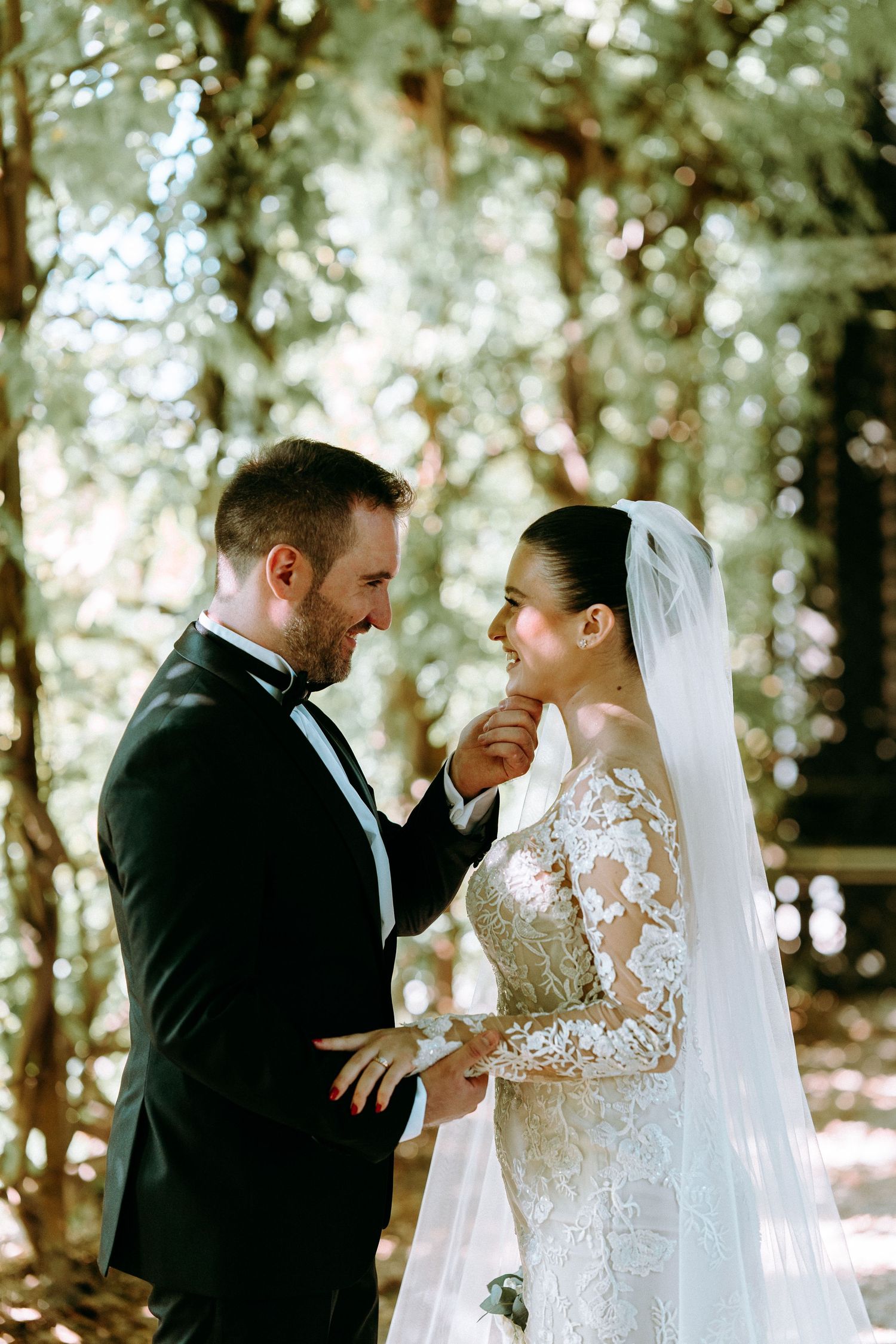 Romantic forest wedding portrait with sunlight filtering through trees.