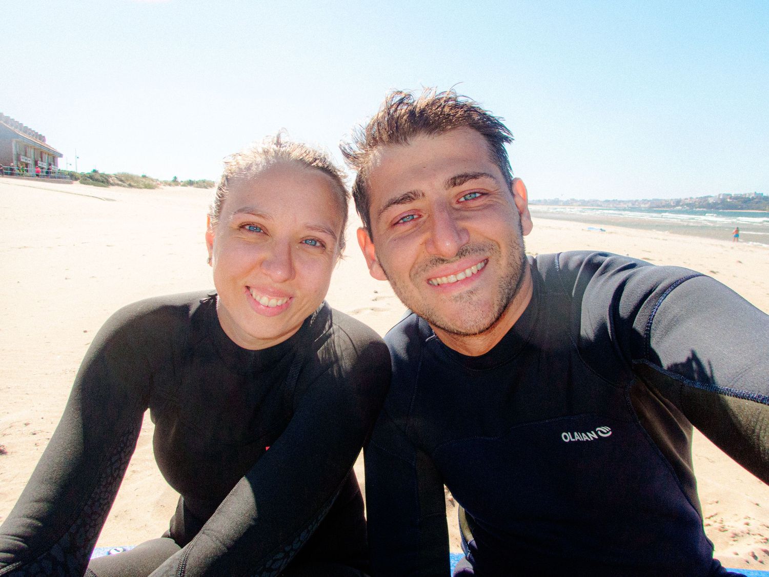 People in black wetsuits smiling together on sunny beach.