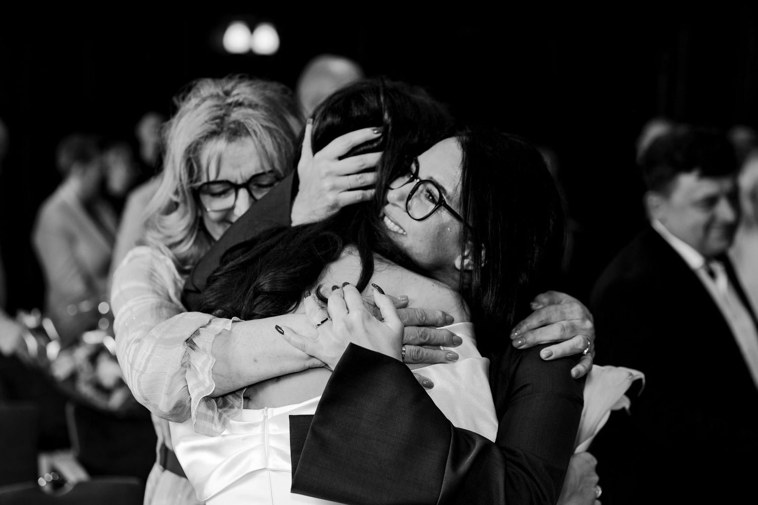 An emotional black and white photo of wedding guests embracing during a reception.