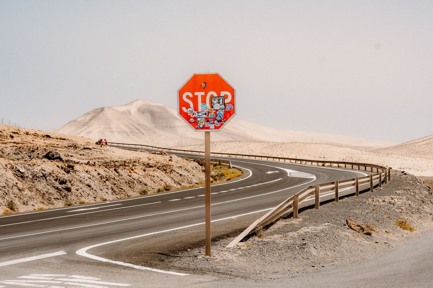 Stop sign on desert highway with winding road and barren mountains in background.