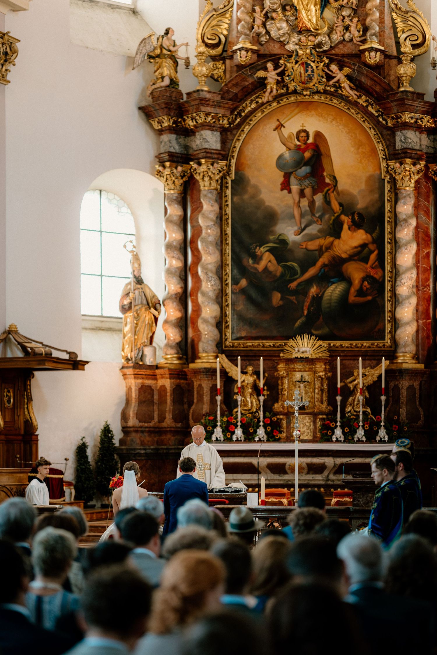 Ornate church interior with golden altar and gathered congregation during a ceremony.