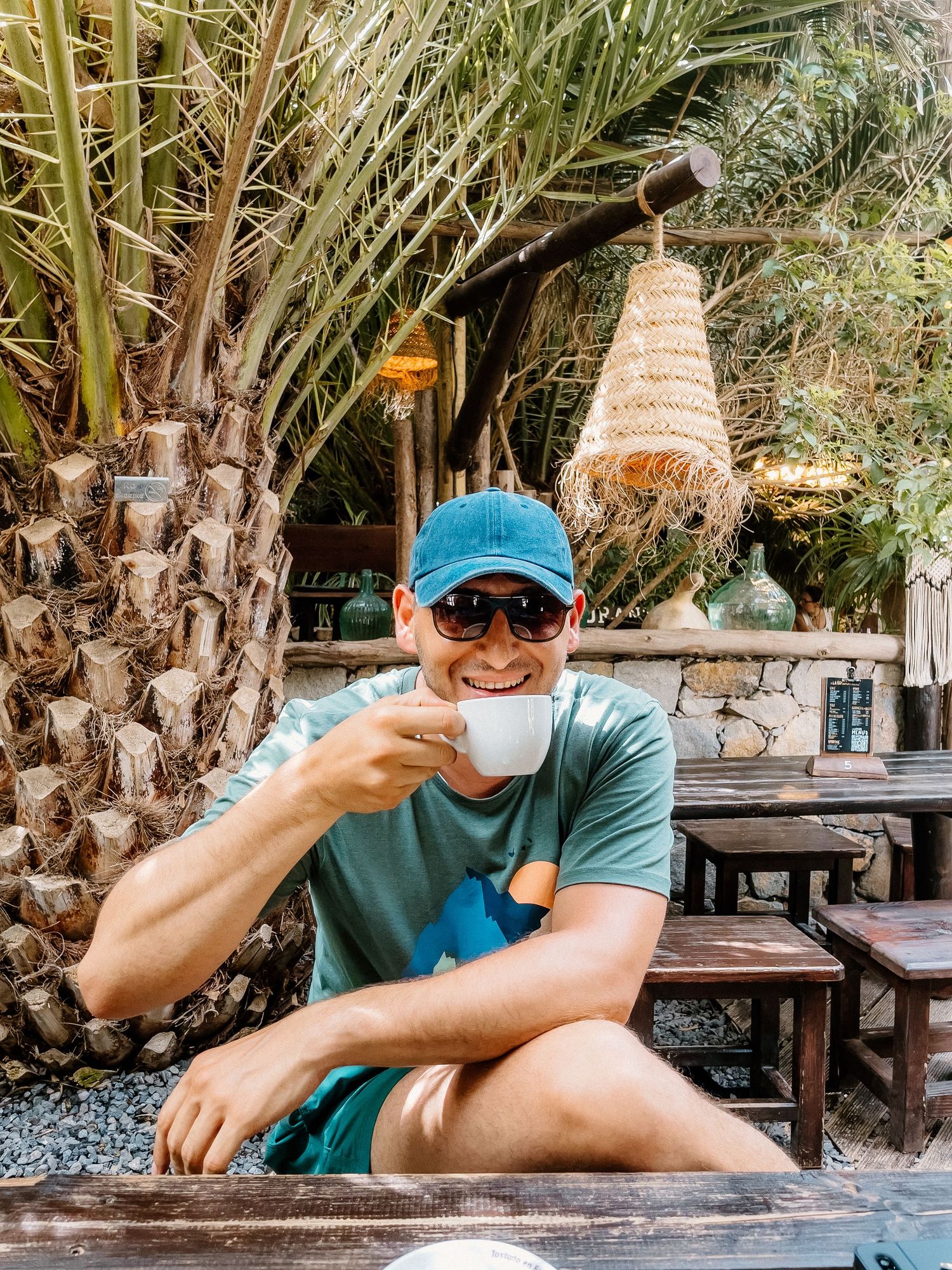 Person enjoying coffee at outdoor cafe surrounded by palm trees.