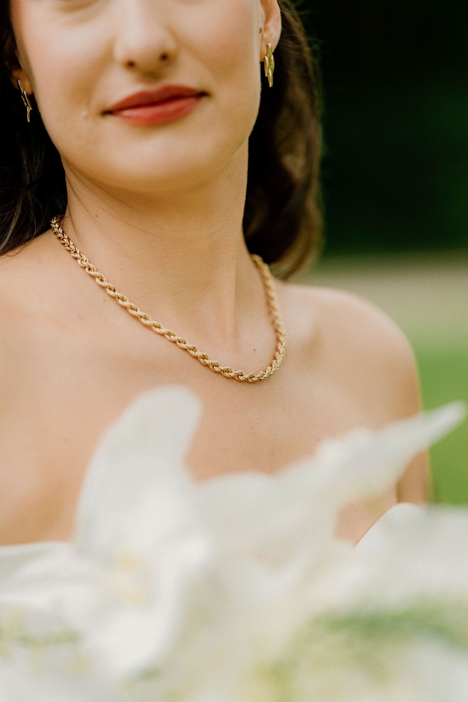 Close-up details of bride wearing gold chain necklace and white dress.