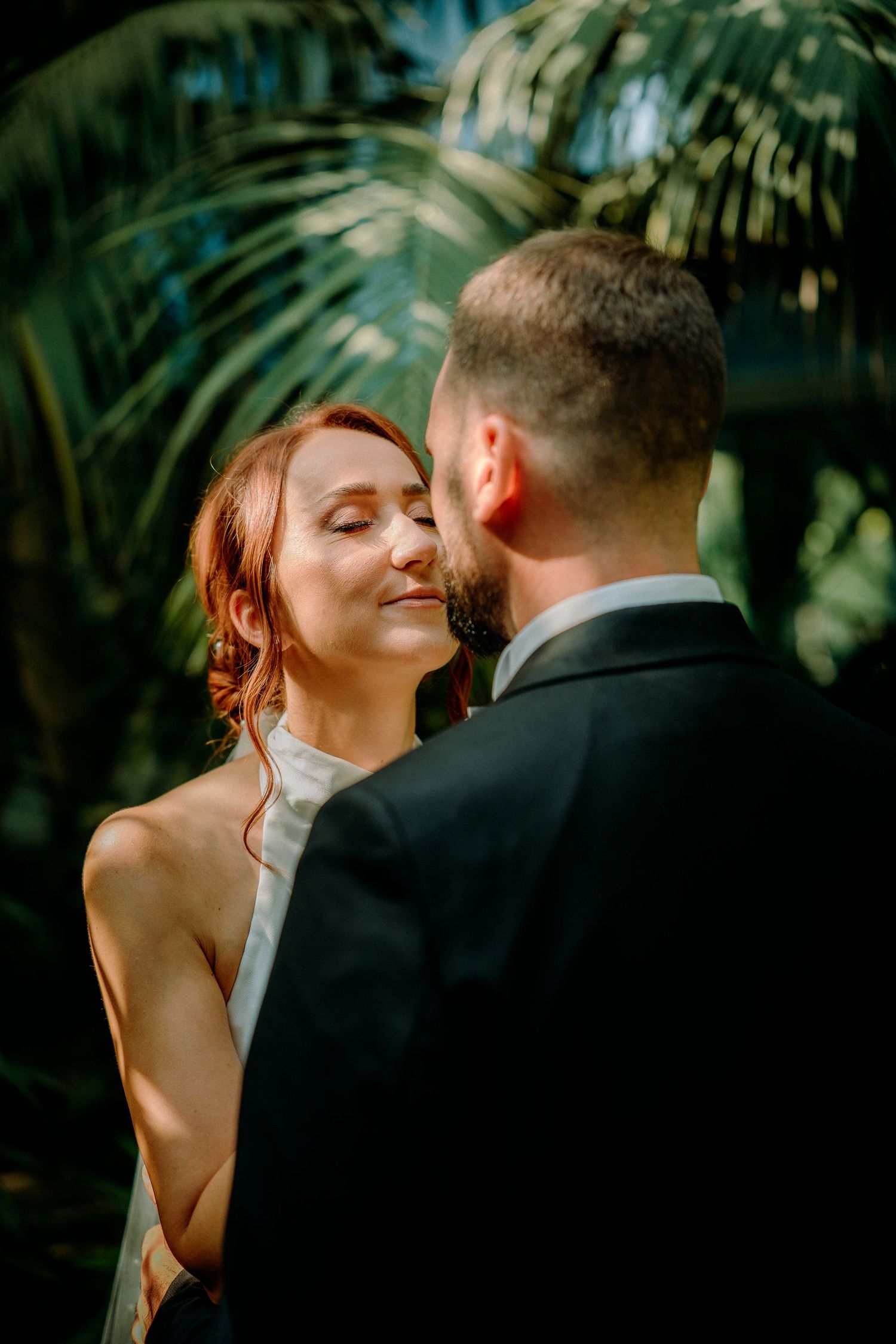 Intimate wedding moments captured through foliage in natural outdoor setting.