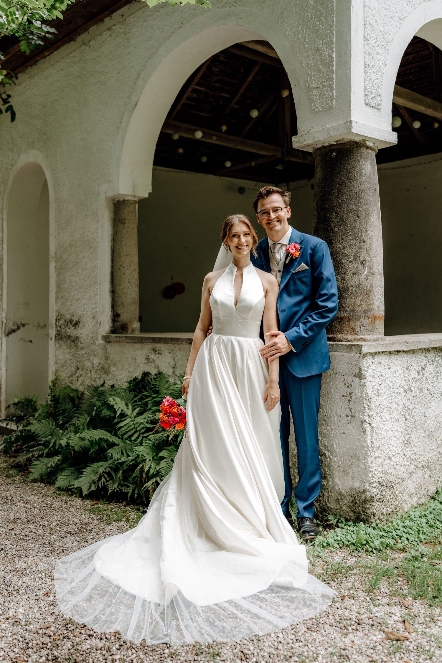 Elegant wedding portraits under white stone archways with trailing greenery and classic architecture.