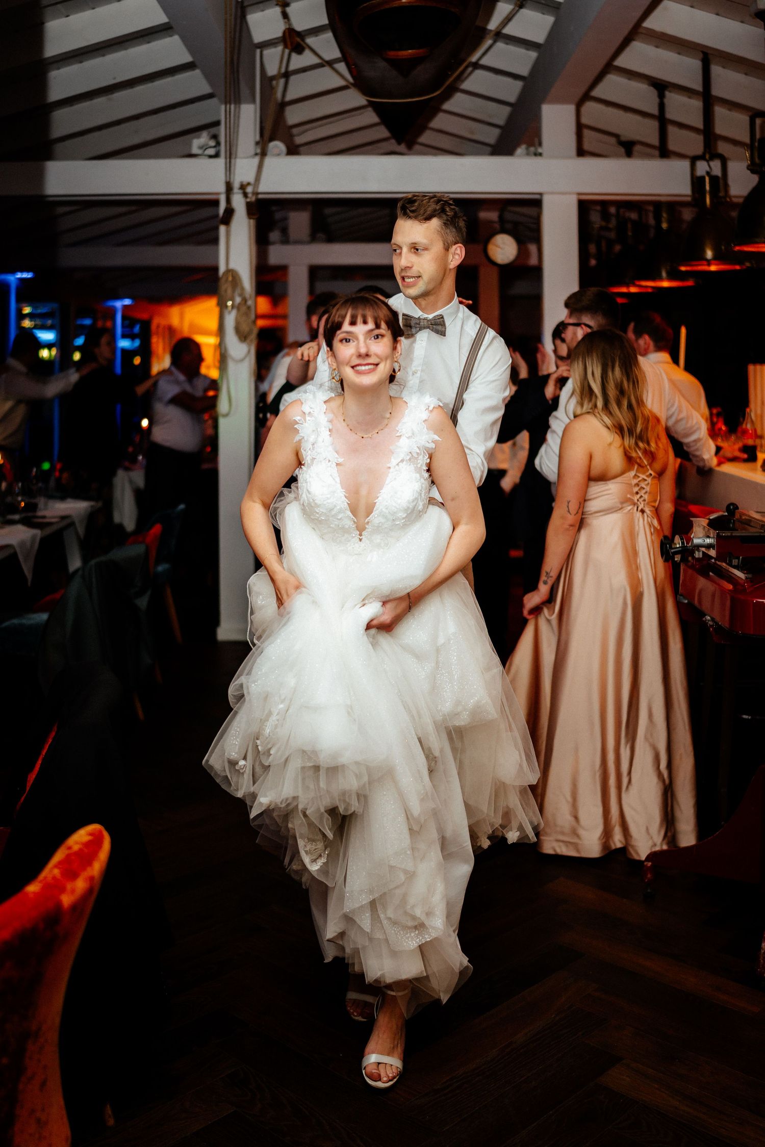 Bride in white tulle gown and groom in suspenders share a joyful dance at elegant wedding reception.