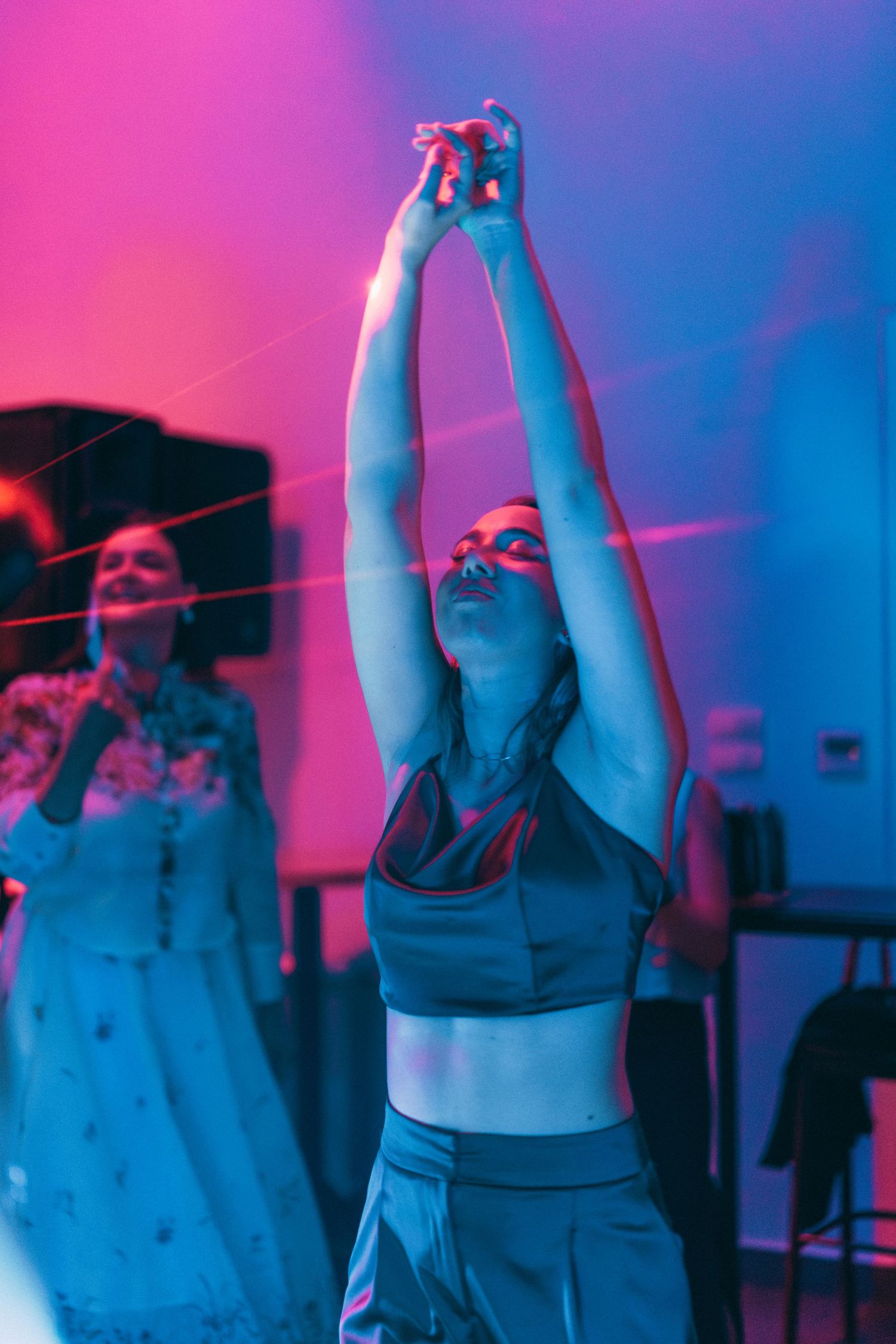 Person dancing with arms raised under vibrant pink and blue lighting at reception.