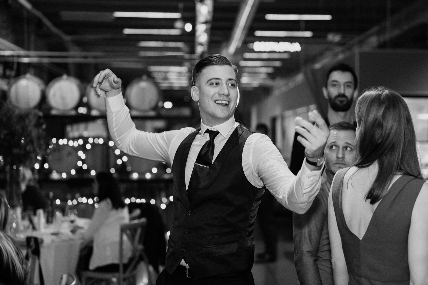Lively wedding reception scene with guests dancing and celebrating under indoor lighting.