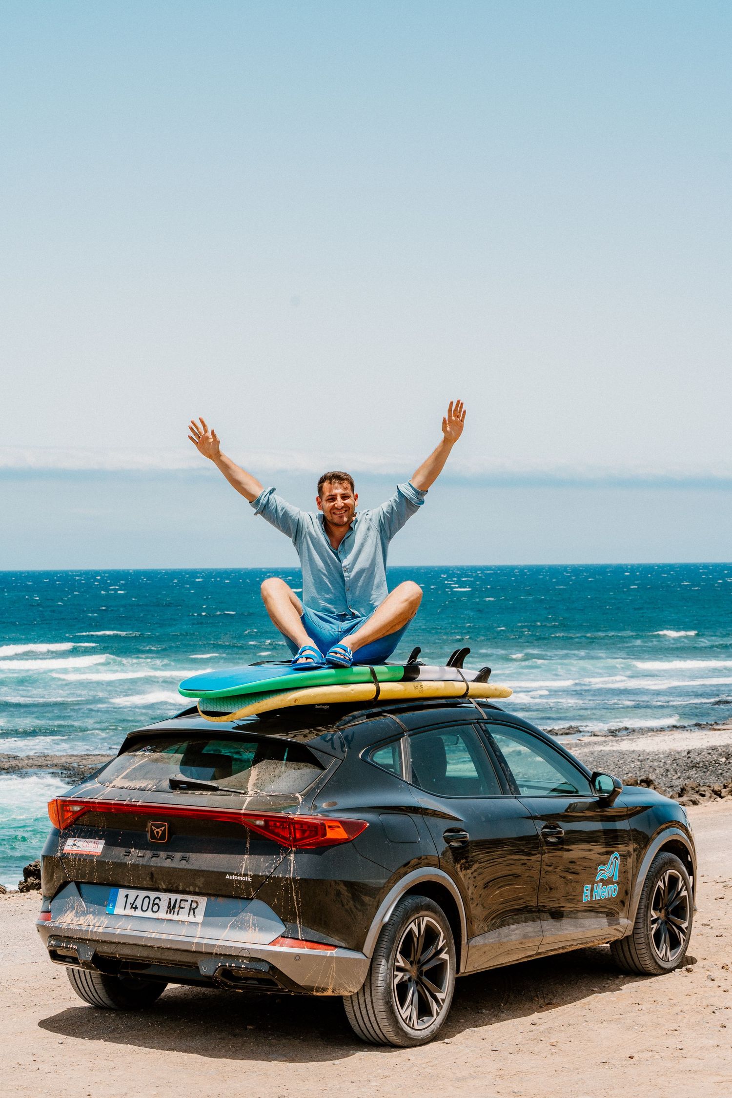 A black sports car parked on a beach with surfboards mounted on top.