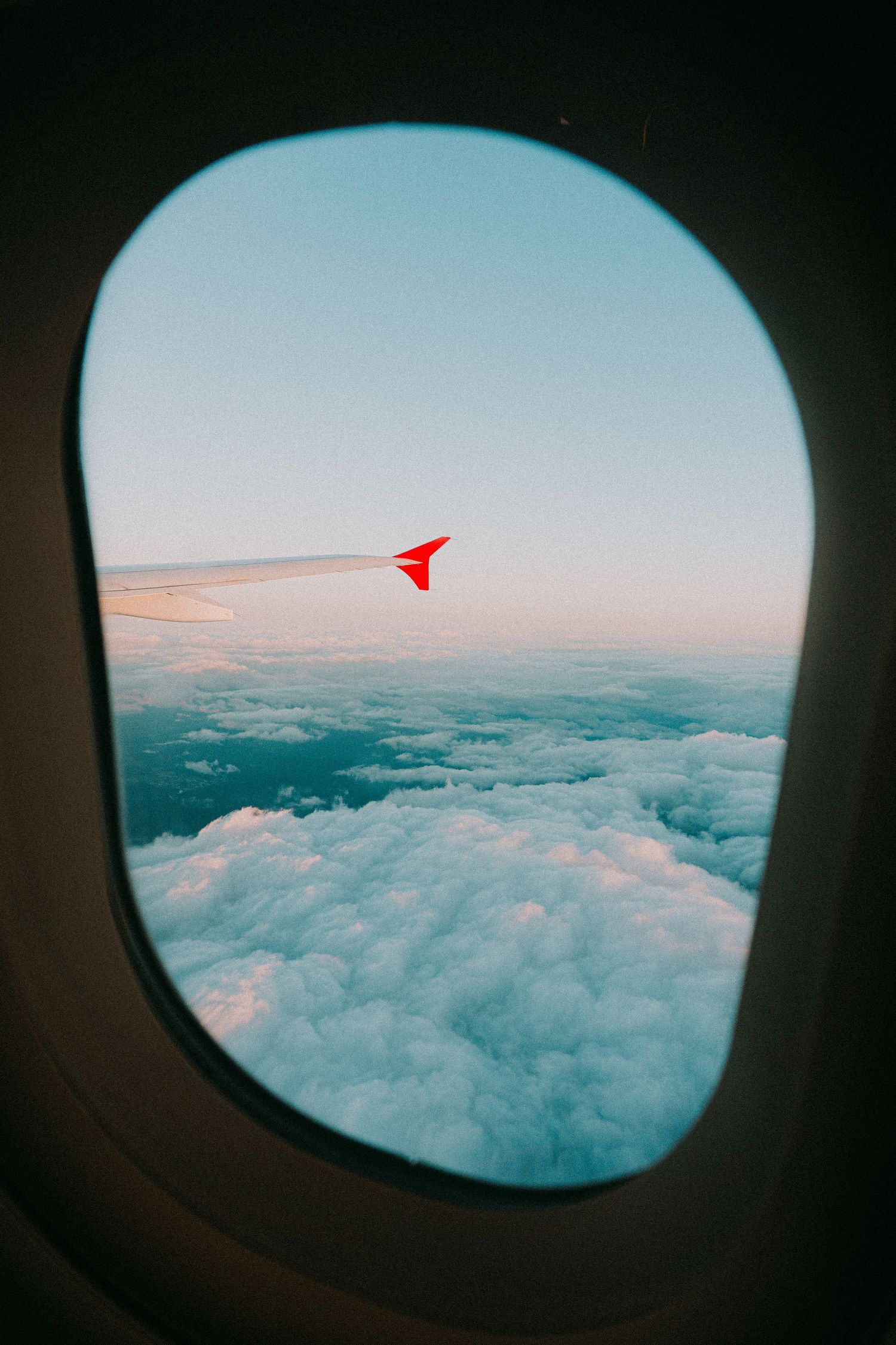 View of fluffy white clouds from an airplane window with a red wingtip visible.