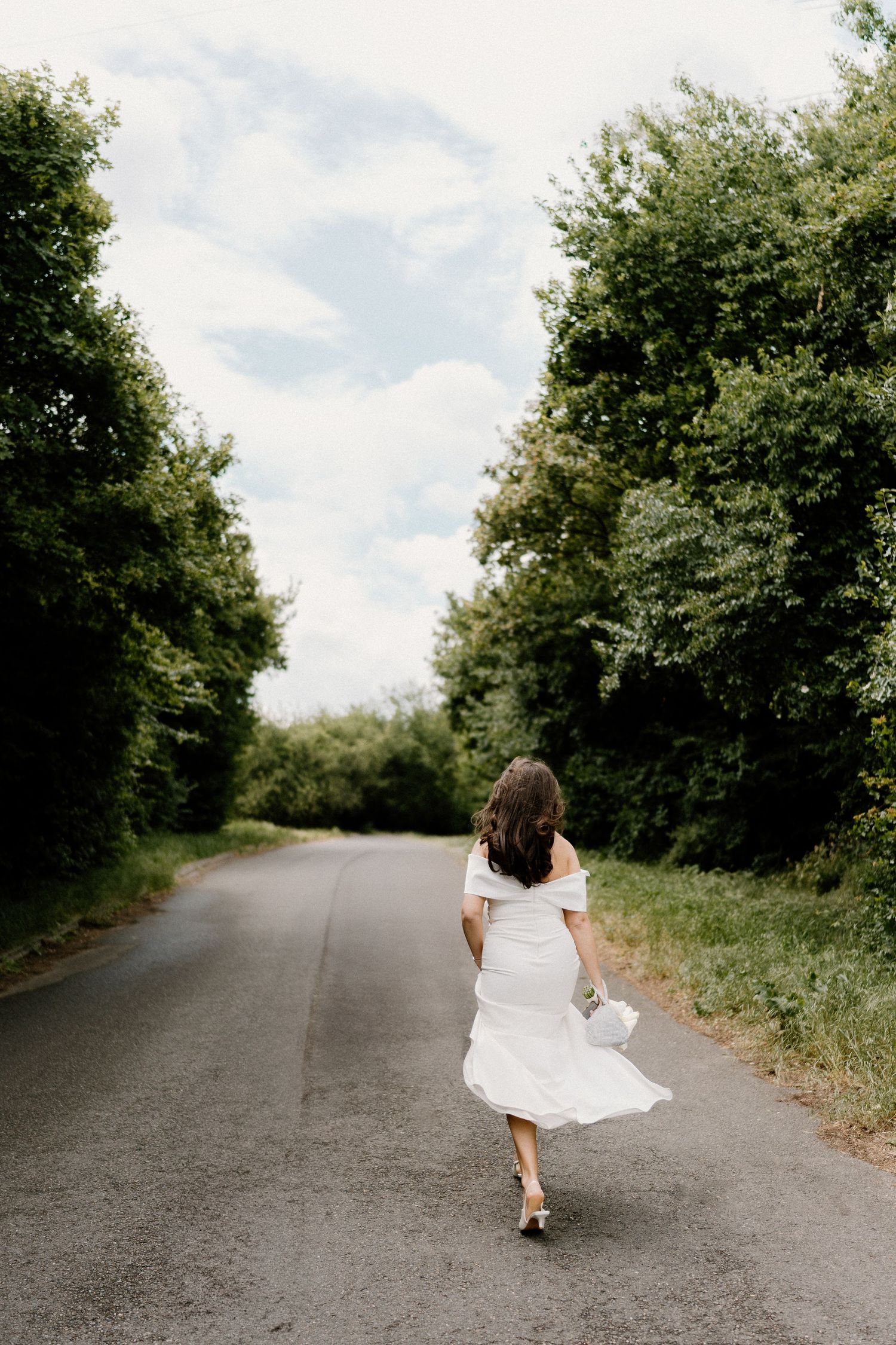 White dress flowing as person walks down a tree-lined country road.