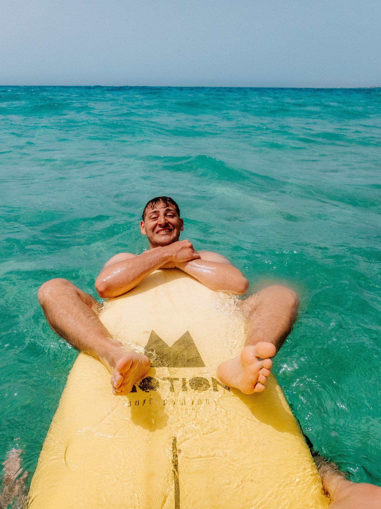 Person floating on yellow raft in crystal clear turquoise ocean waters.