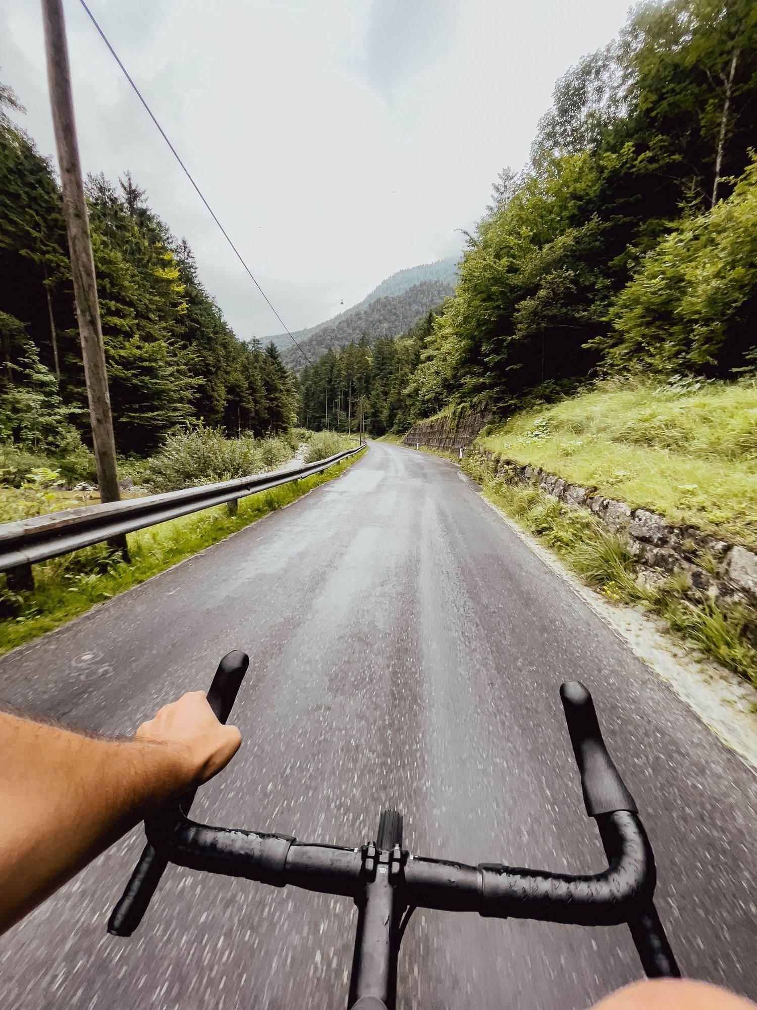 Point-of-view shot of cycling on a winding mountain road surrounded by lush green forest.