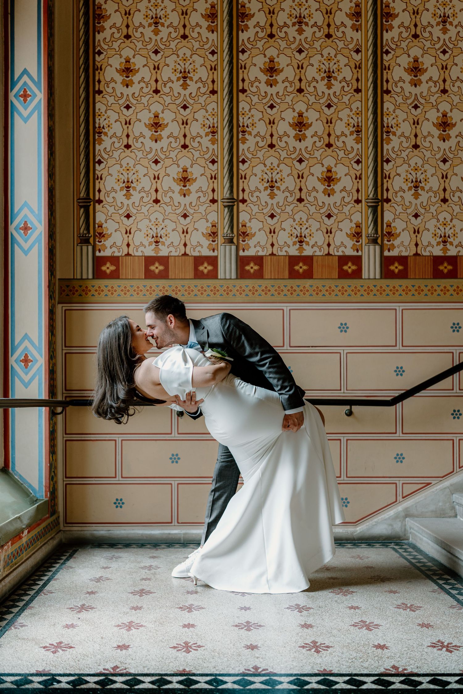 Romantic wedding couple dips and poses in an elegant vintage room with patterned wallpaper.